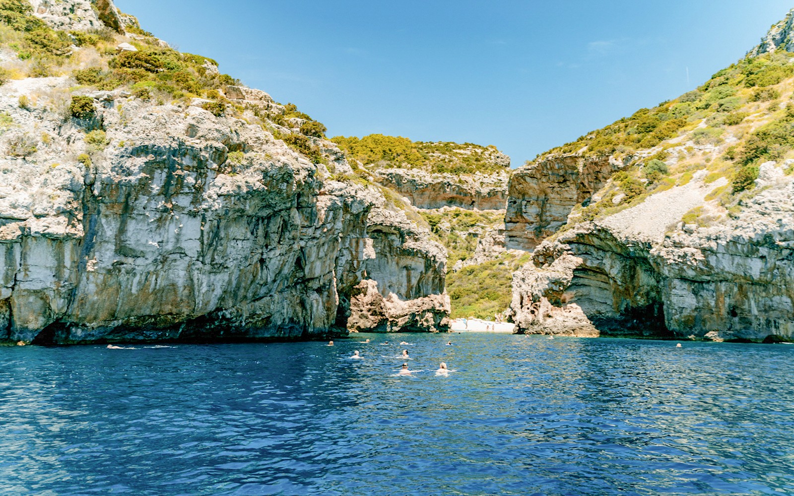 Blick auf die Stiniva-Bucht mit Schwimmern im klaren blauen Wasser, umgeben von felsigen Klippen, Vis-Insel, Kroatien.