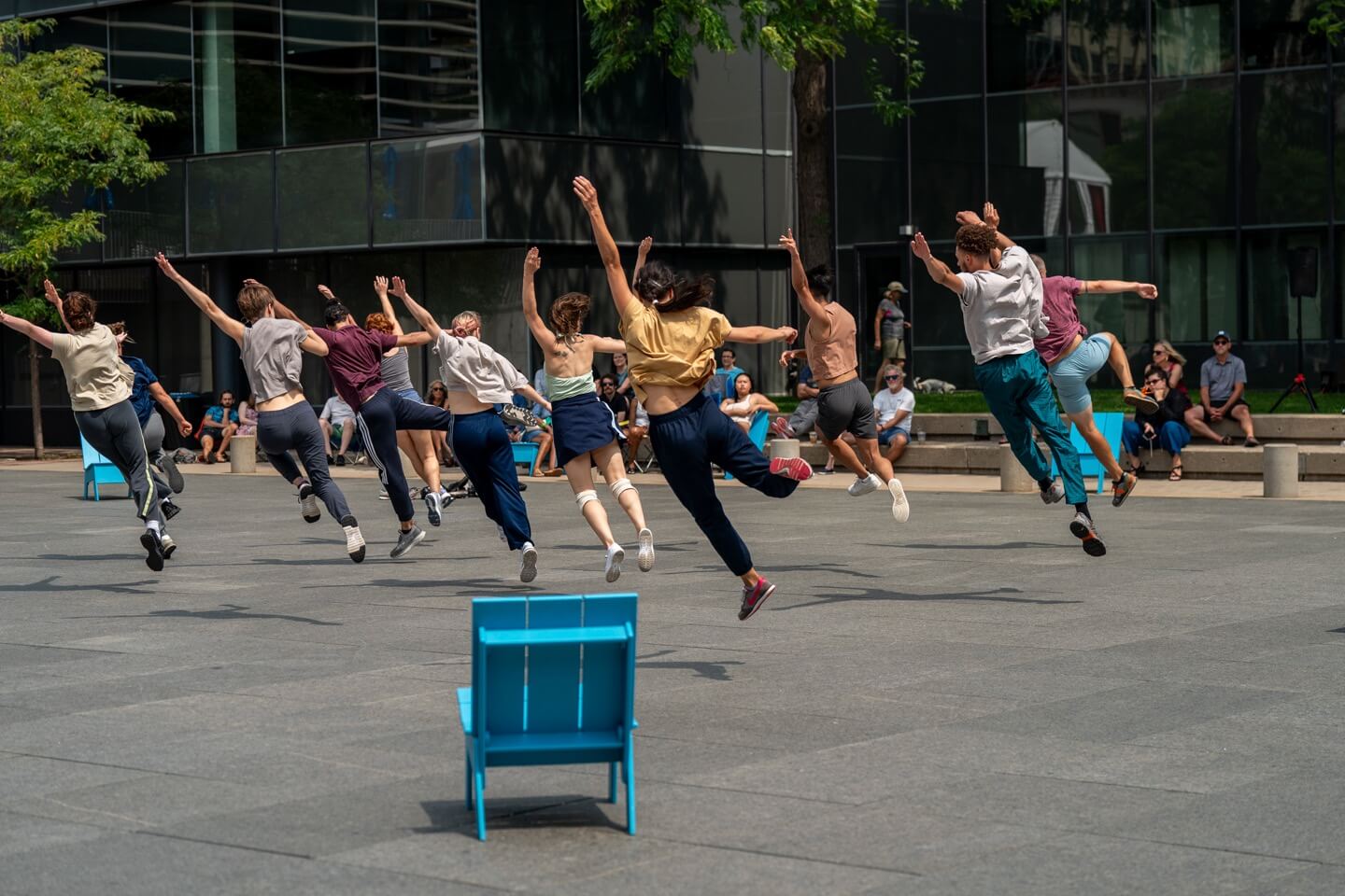 A group of students leaps energetically in an outdoor dance class next to a bright blue chair. Photo by Bill Cameron.