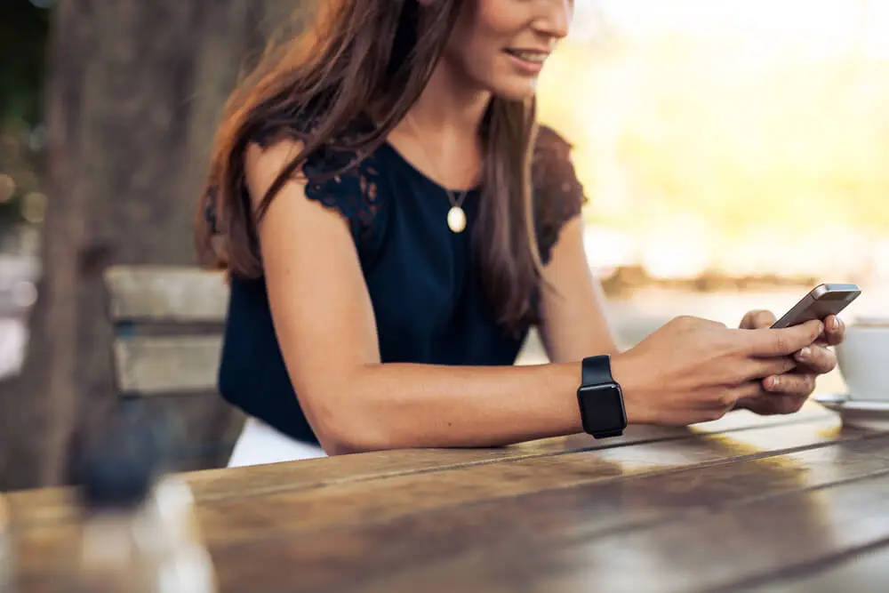 Woman sitting at an outdoor table using a smartphone with a smartwatch on her wrist