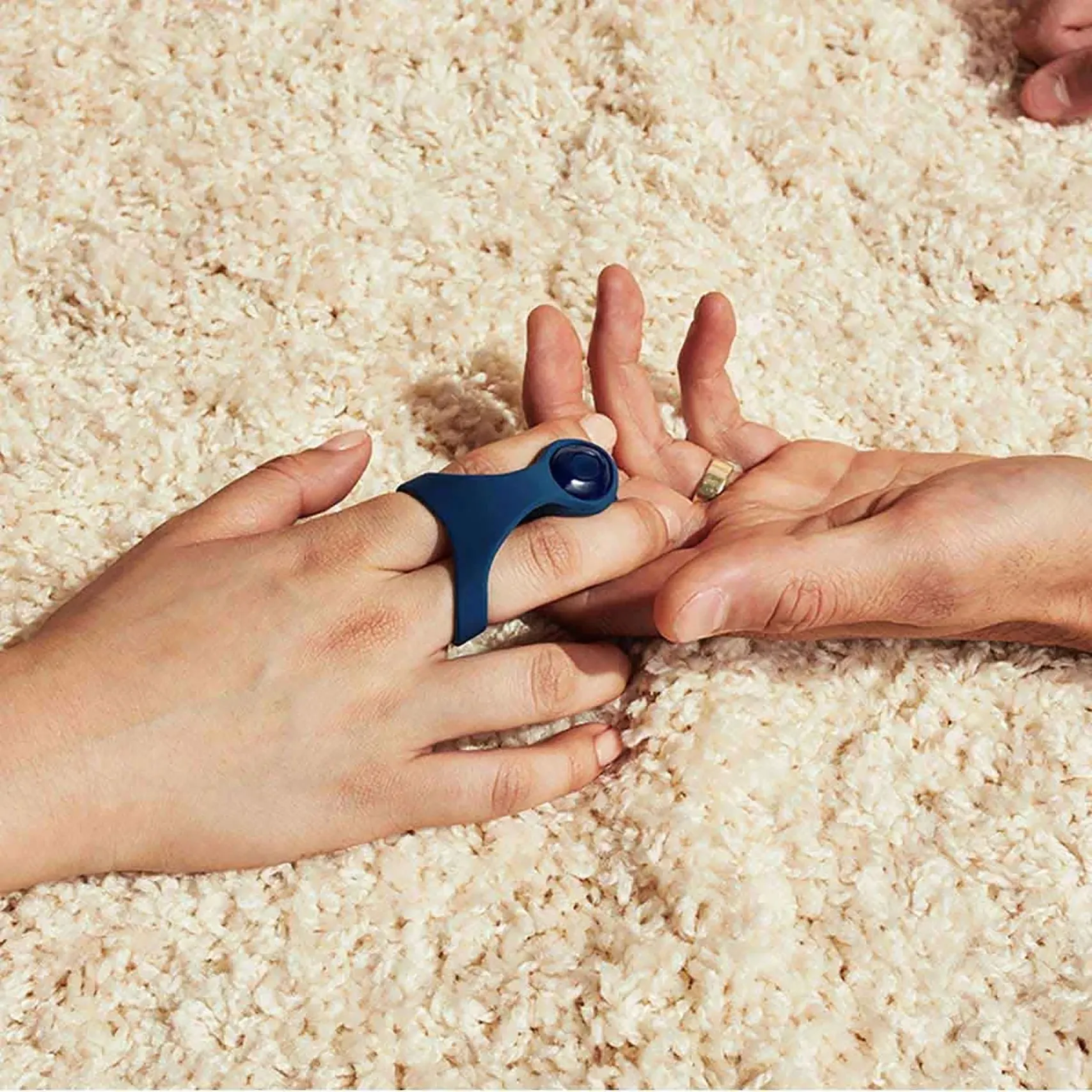 Hands demonstrating a dark blue Dame sexual wellness device on a cream rug