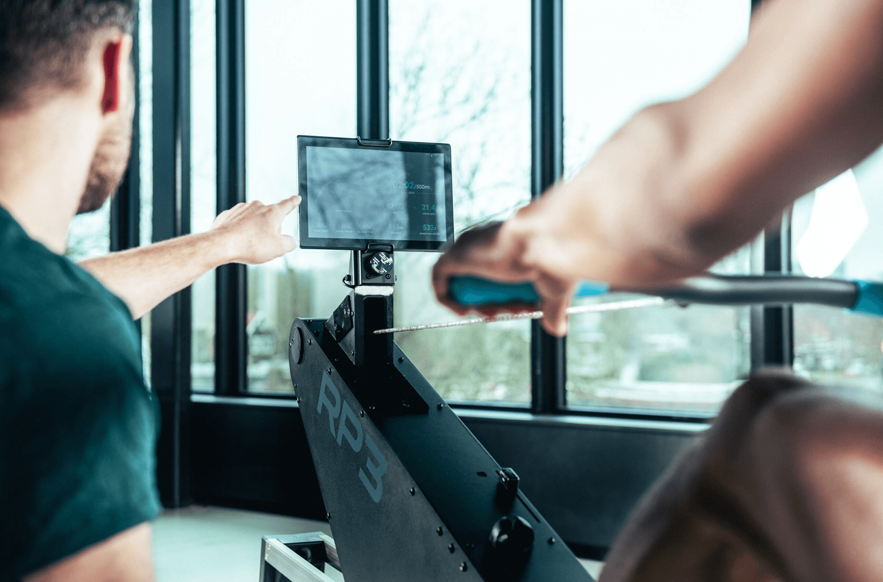 Coach helping an athlete understand the data from the tablet on a rowing machine.
