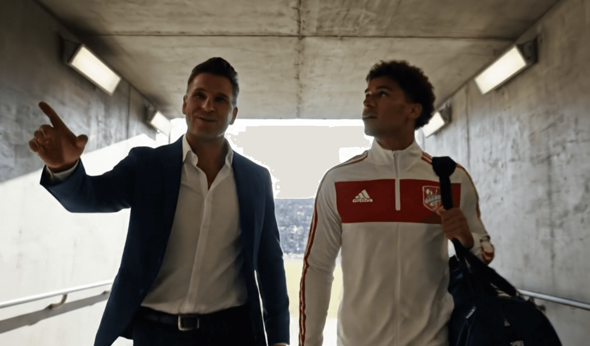 Representante y jugador caminando por el túnel del estadio, platicando.