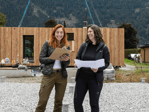 Young woman with short, dark hair and a yellow sweater looks serious, surrounded by hands holding smartphones, conveying intrusion and tension.