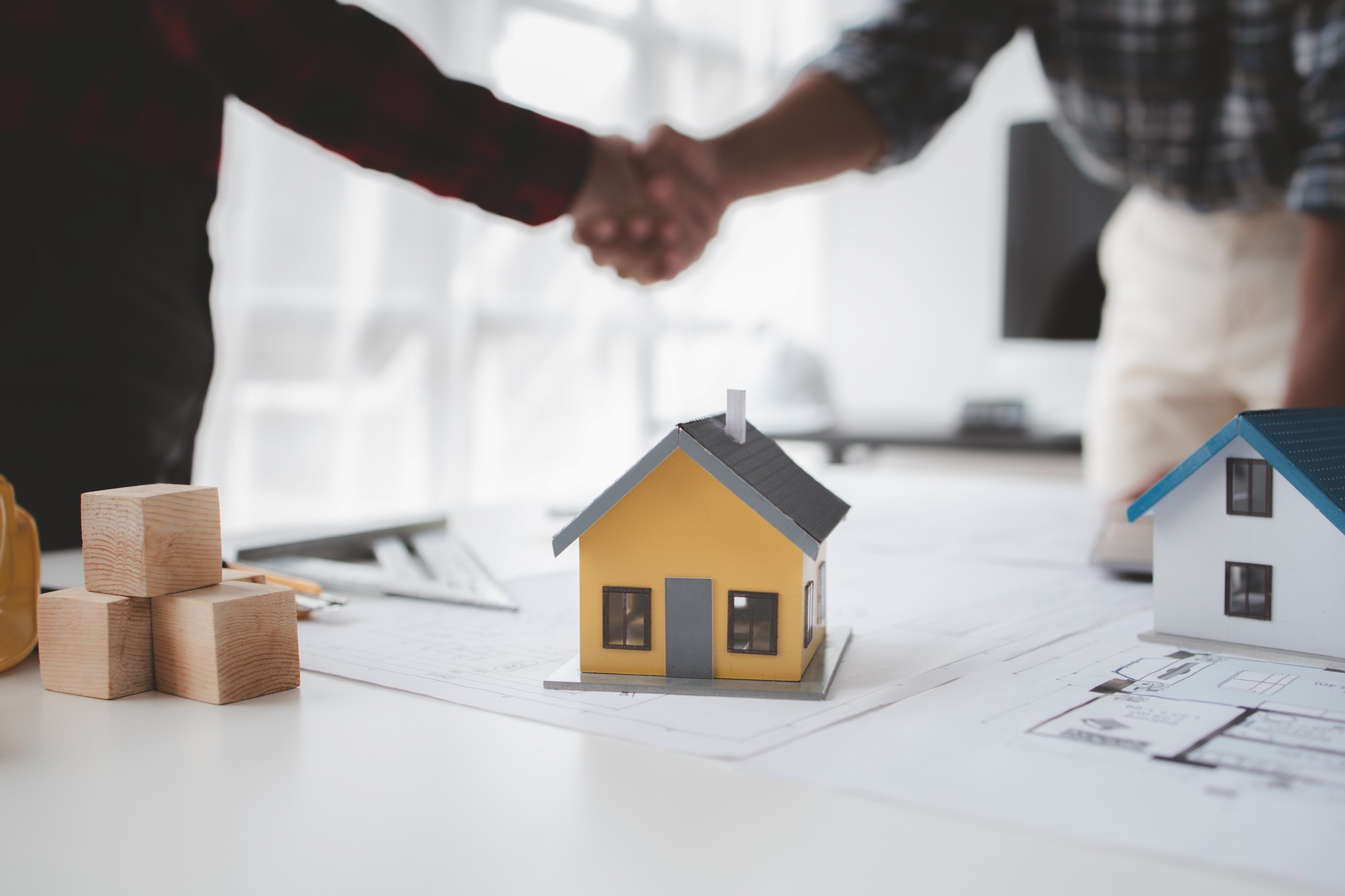 Handdruk bij hypotheekadvies met modelhuis en bouwtekeningen op tafel