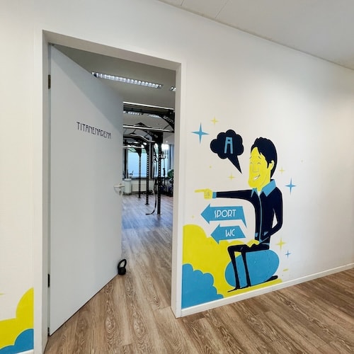 Ein Blick in unseren Sportraum vom Flur aus. Der Sportraum heißt Titanenarena und ein Comic Avatar weist hinein.