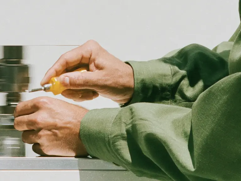 Person in green workwear using a screwdriver on a metal machine.