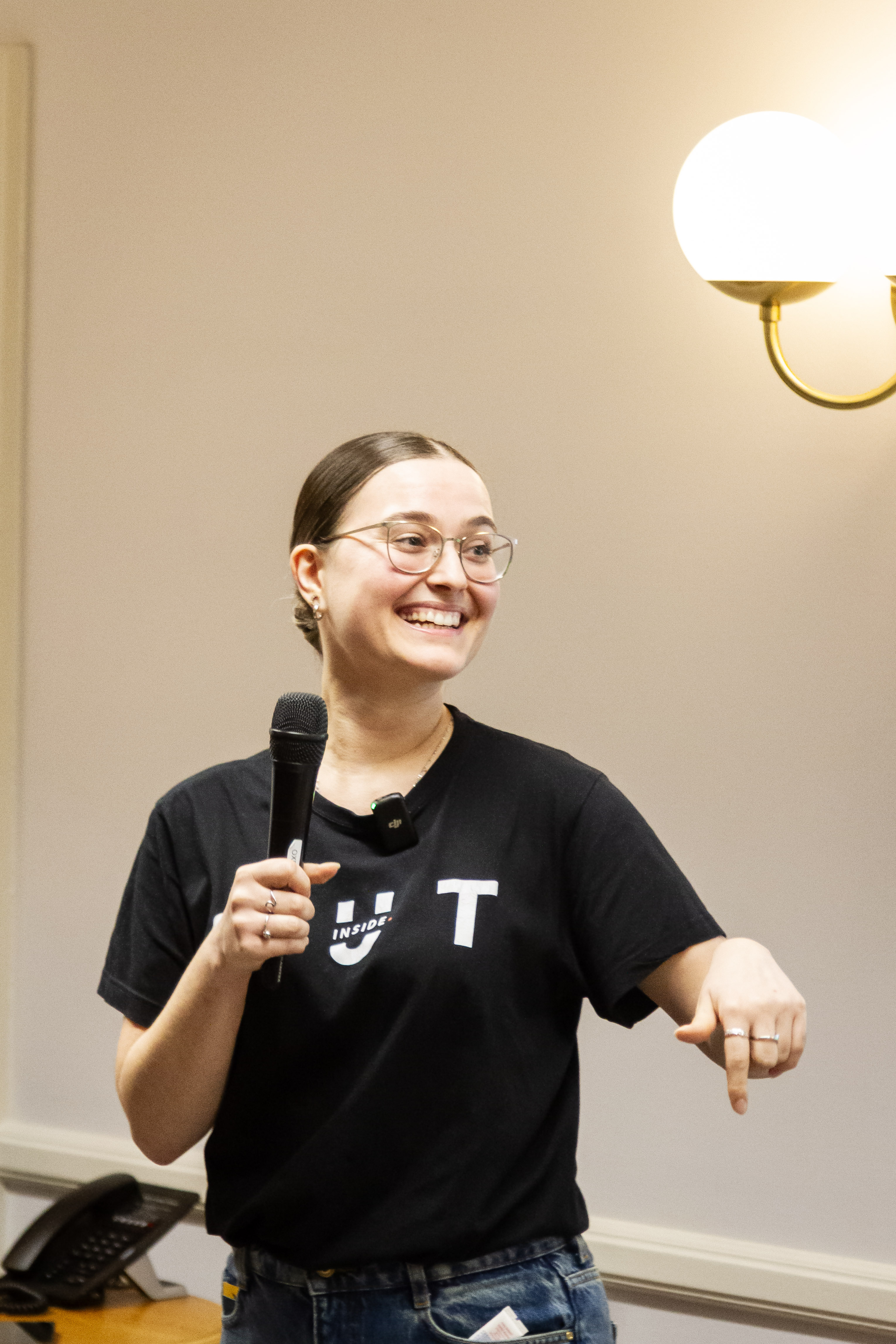 Woman in black t-shirt with "OUT" logo, speaking into microphone and smiling.
