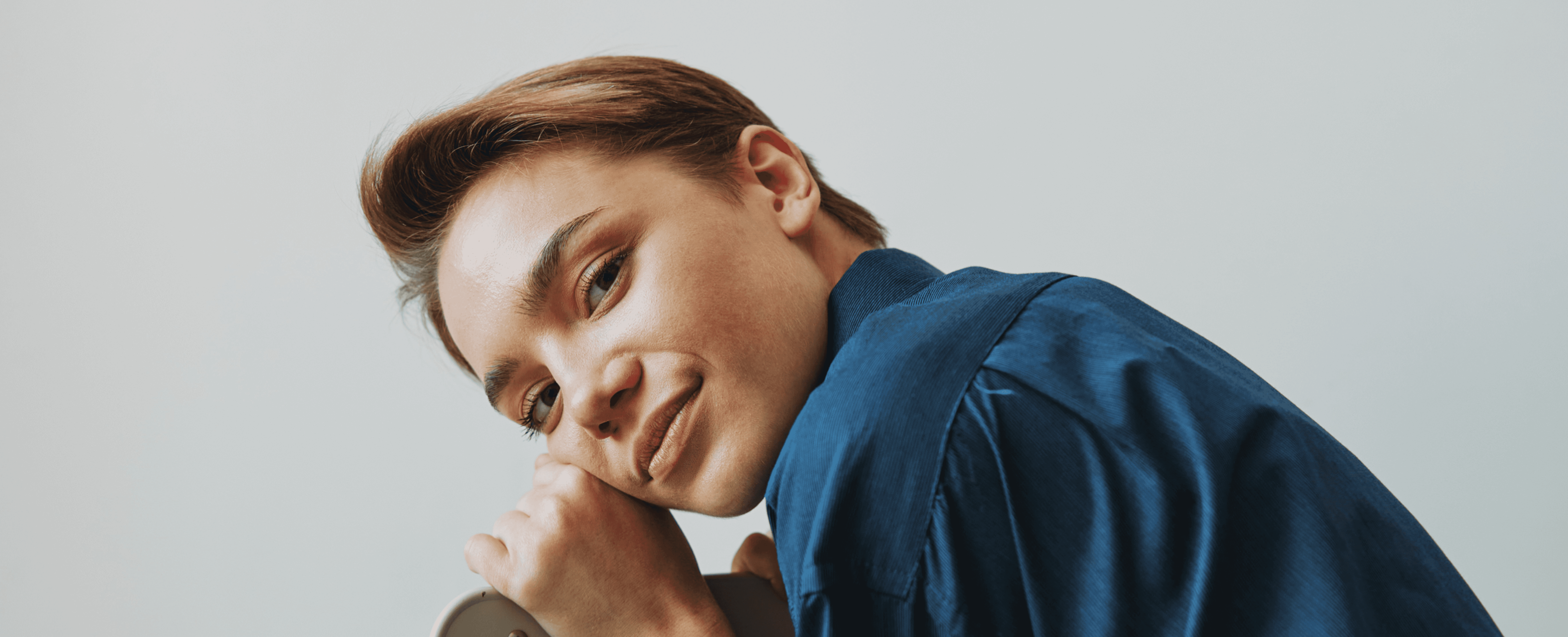 Portrait of young woman leaning on chair in blue shirt, studio shot,.
