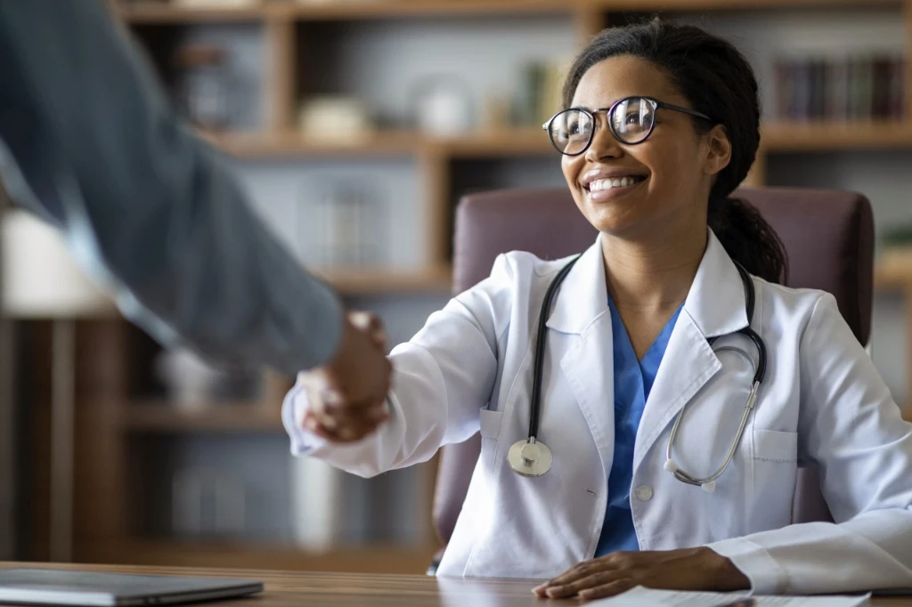 Ethnic ffemale doctor shaking hands with someone out of frame on the left.