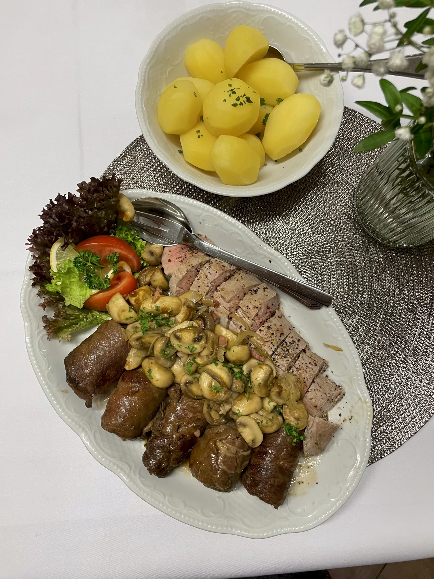 Teller mit gebratenem Fleisch, Kartoffeln und Sauce. Dazu Salat und dekoratives Grün.