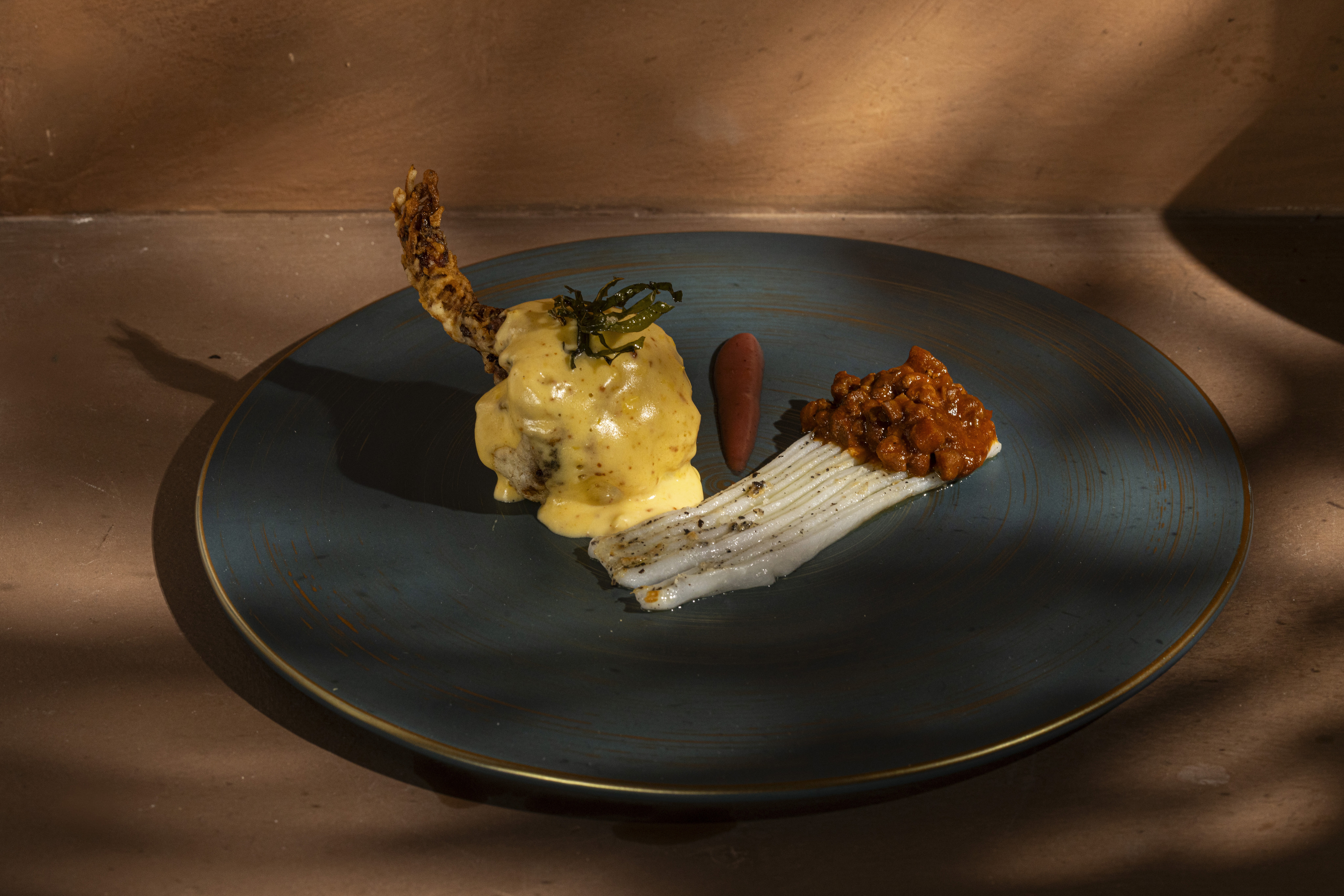 White plate with roasted chicken served in a golden sauce with herbs and capers, placed on a terrazzo tabletop in sunlight.
