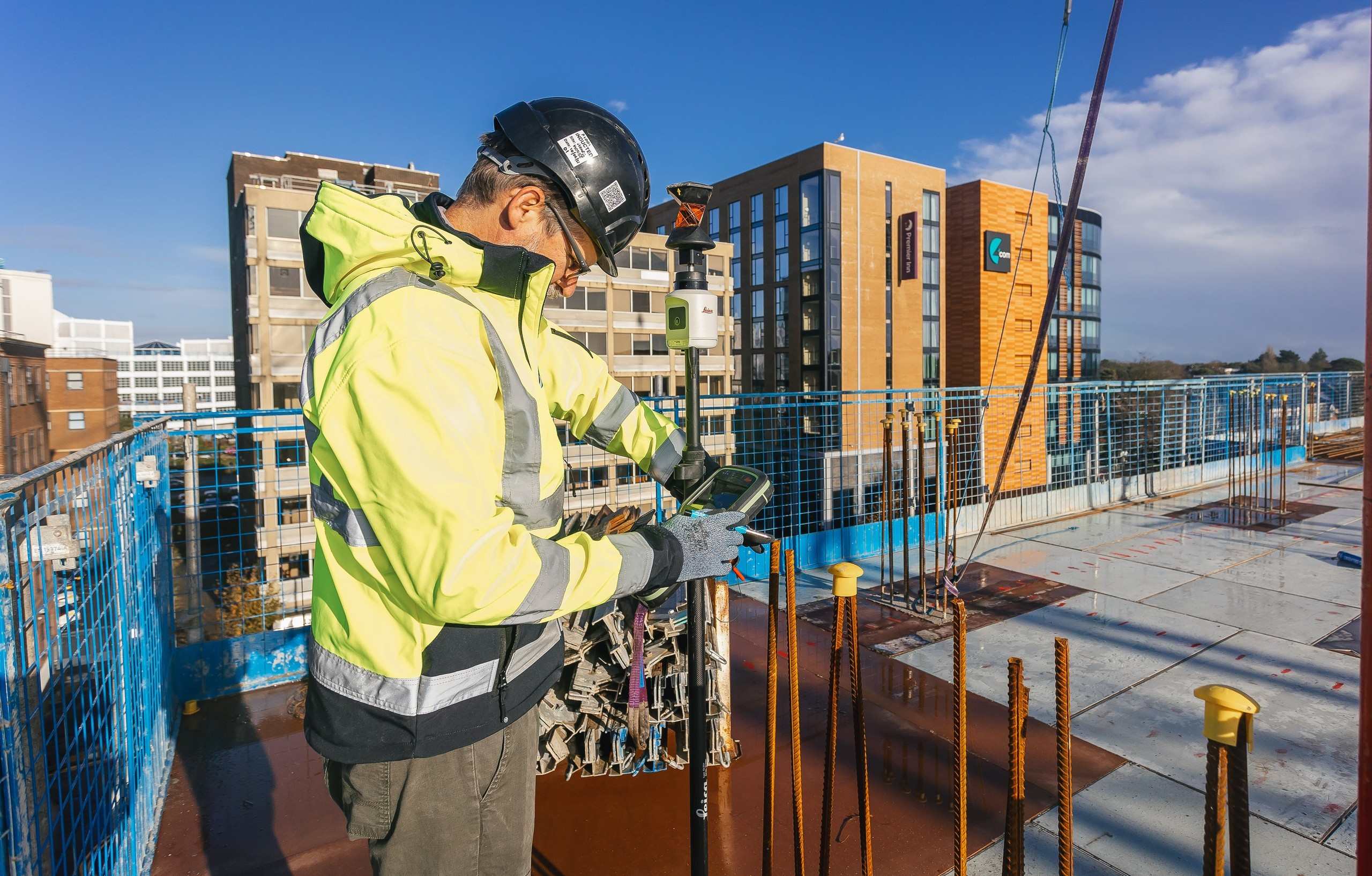 A surveyor looking at an ipad wearing PPE stands on the roof of a building under construction