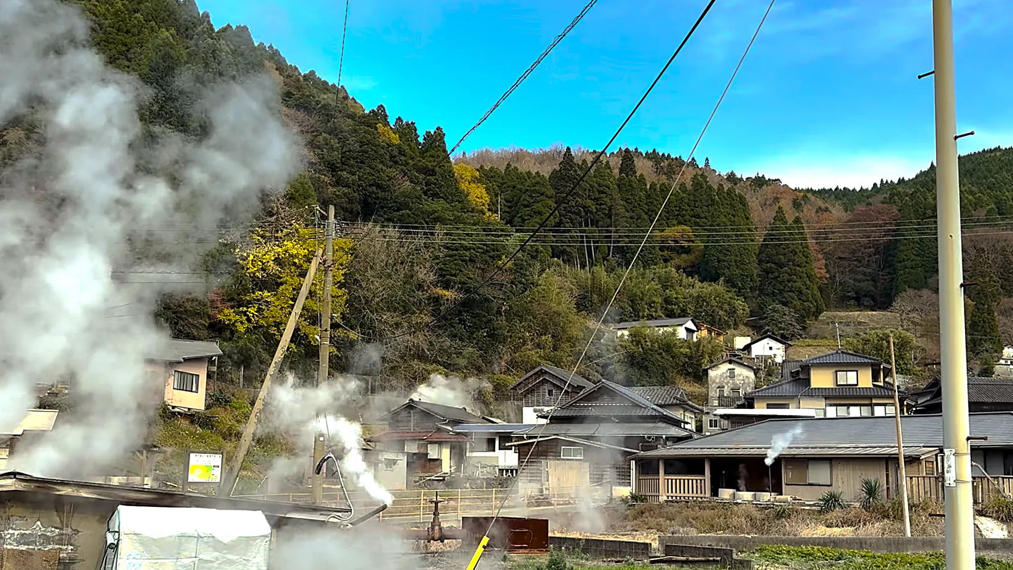 A wide view of the steam village at Waita near Kurokawa Onsen, roofs below a cedar slope
