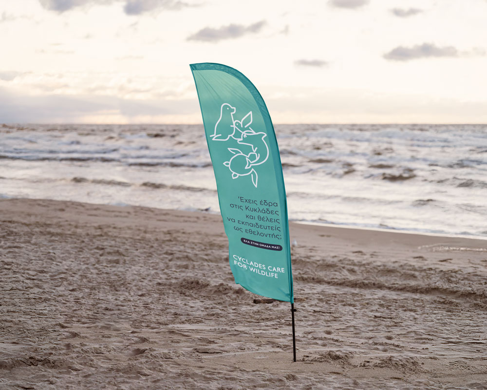 Application of the Cyclades Care for Wildlife identity on outdoor beach signage, adapted to the natural environment