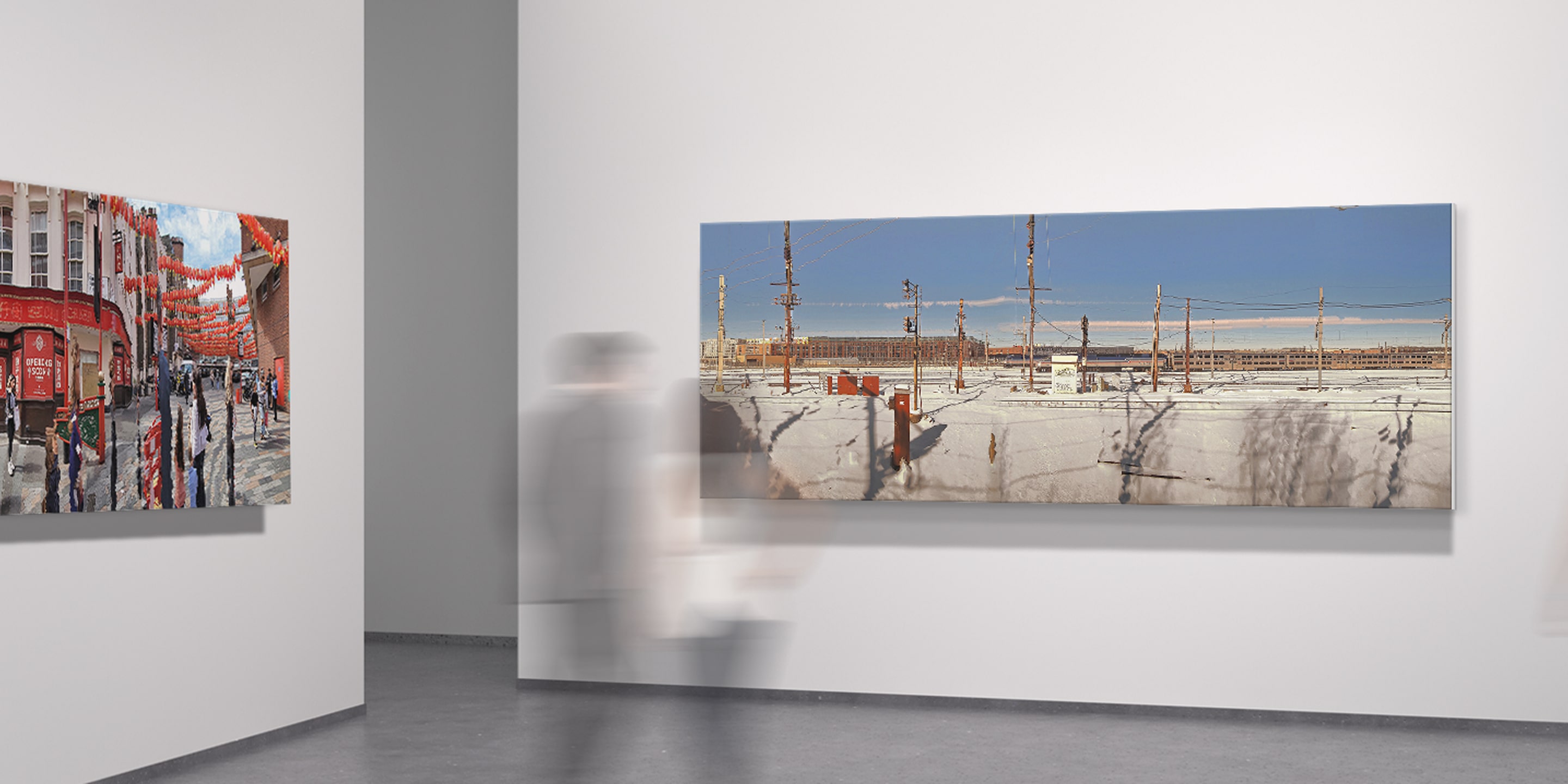 Blurred visitors moving through a gallery space lined with large panoramic photographs of urban and natural environments.
