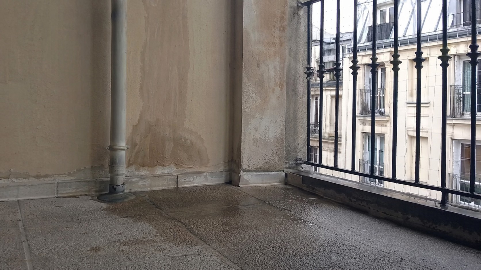 Photo Panasonic GH4 montrant une fuite de balcon ou terrasse en copropriété à Paris, extérieur d’immeuble sans présence humaine, traces d’infiltration d’eau sur façade et sol, ambiance documentaire réaliste, cadrage imparfait, lumière naturelle, image illustrative pour diagnostic et responsabilité des travaux