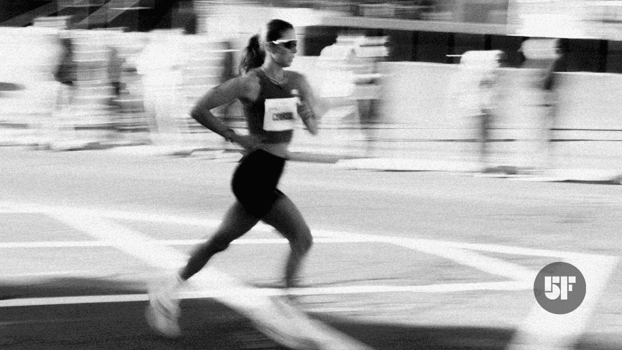 A black and white, motion-blurred photograph of a female athlete running intensely during a race