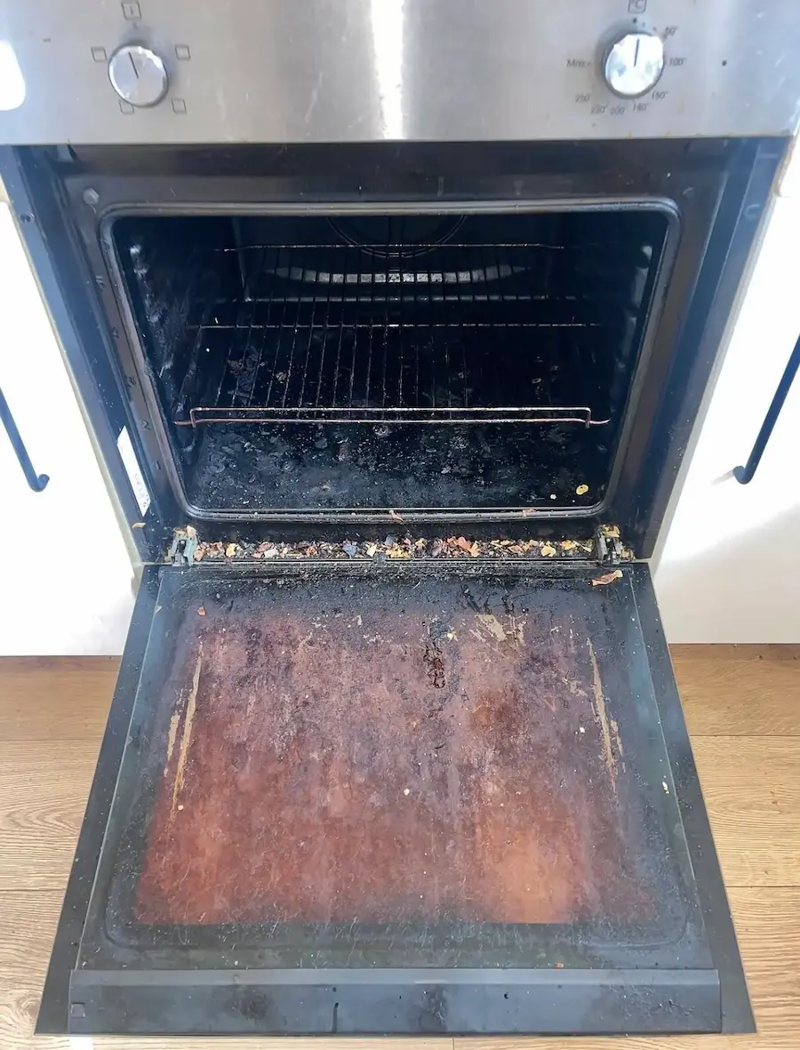 Interior of an oven with a heavily stained and greasy glass door, before a professional deep clean.