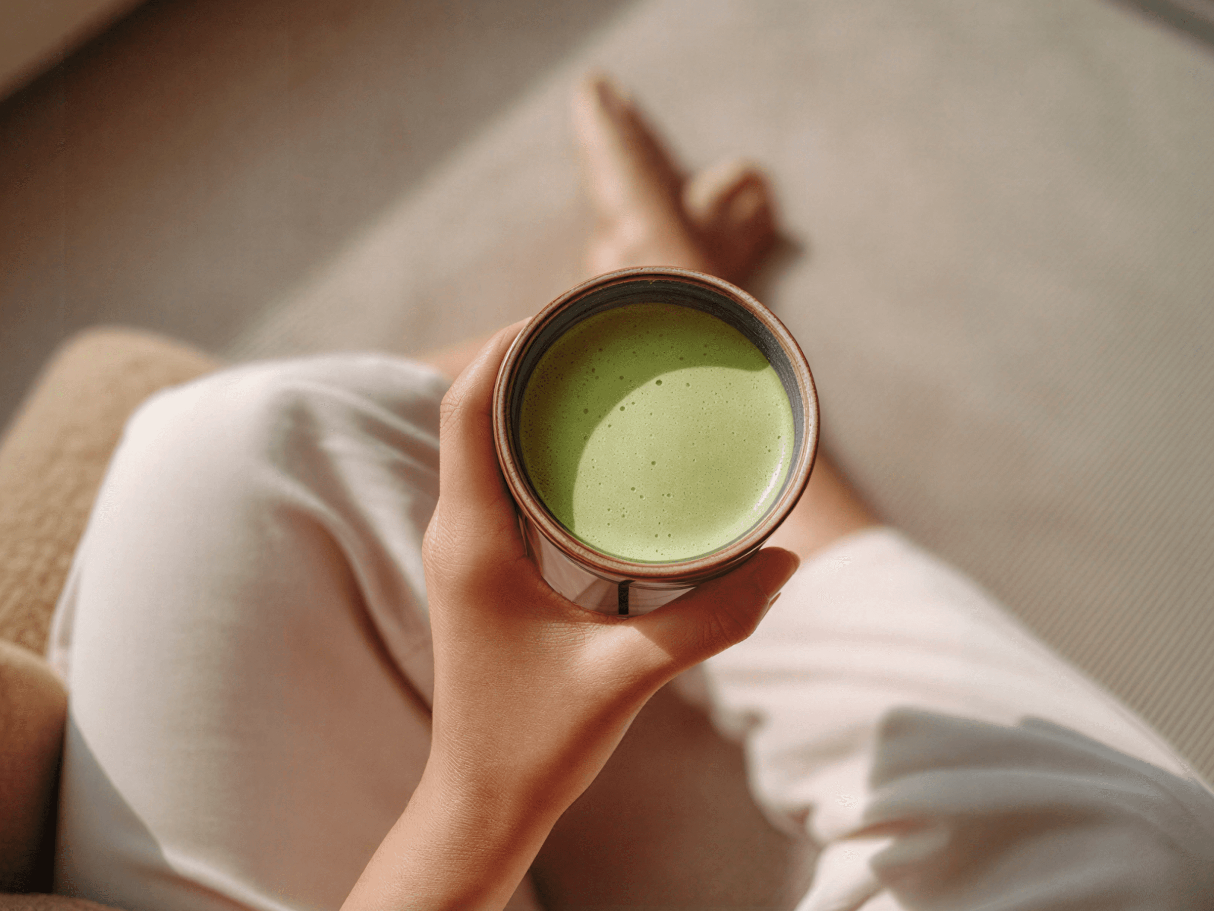 Hand holding a ceramic matcha bowl with frothy matcha while seated in white clothing