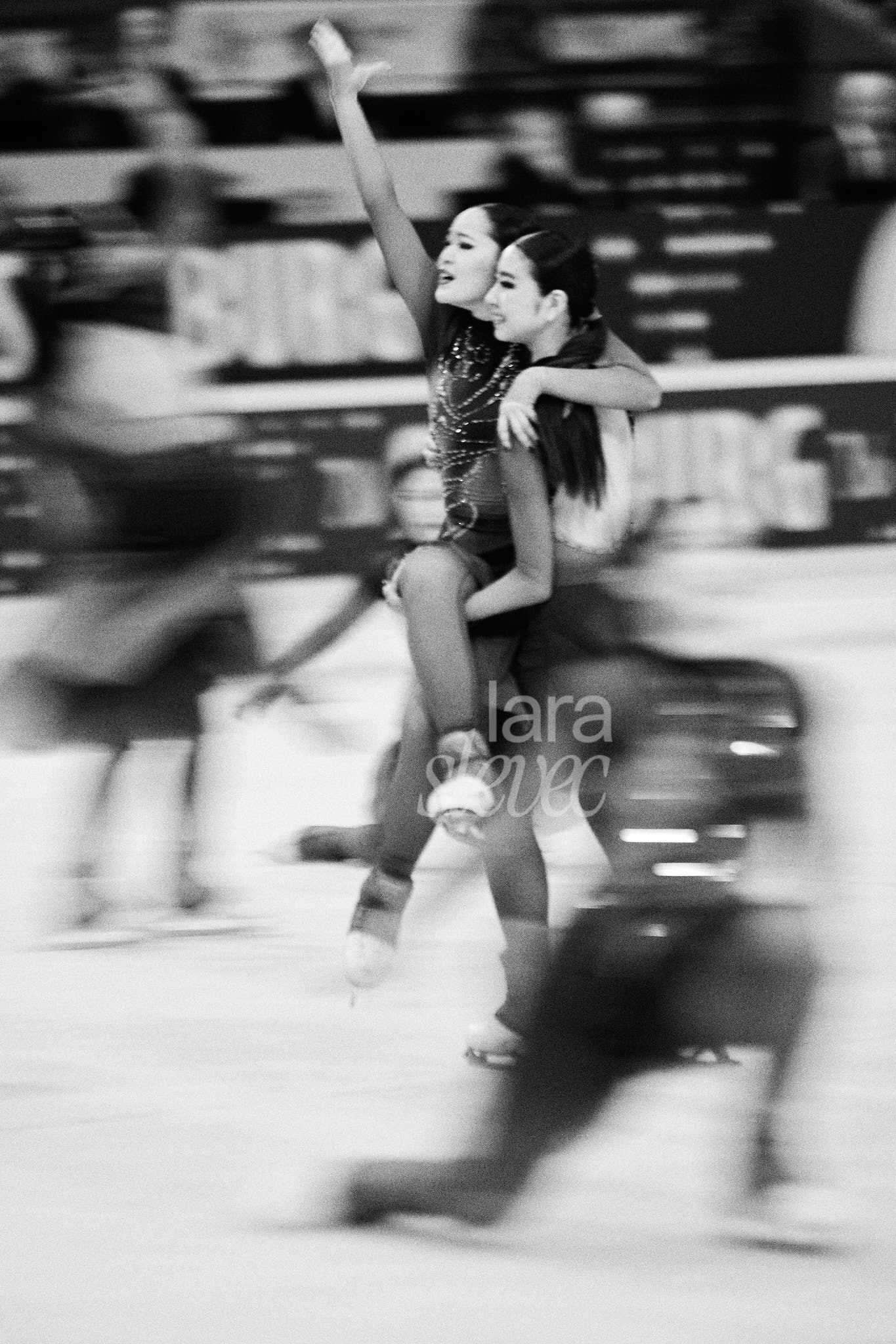 Schwarz- Weiß Bild im Analog-Stil. Eine Hebung von zwei Synchroneiskunstläuferinnen. Drei weitere sind in Bewegungsunschärfe zu erkennen. Team Jingu Ice Messengers. ISU Synchronized Skating Championships 2026 in Salzburg. Fotografiert von Lara Slevec.