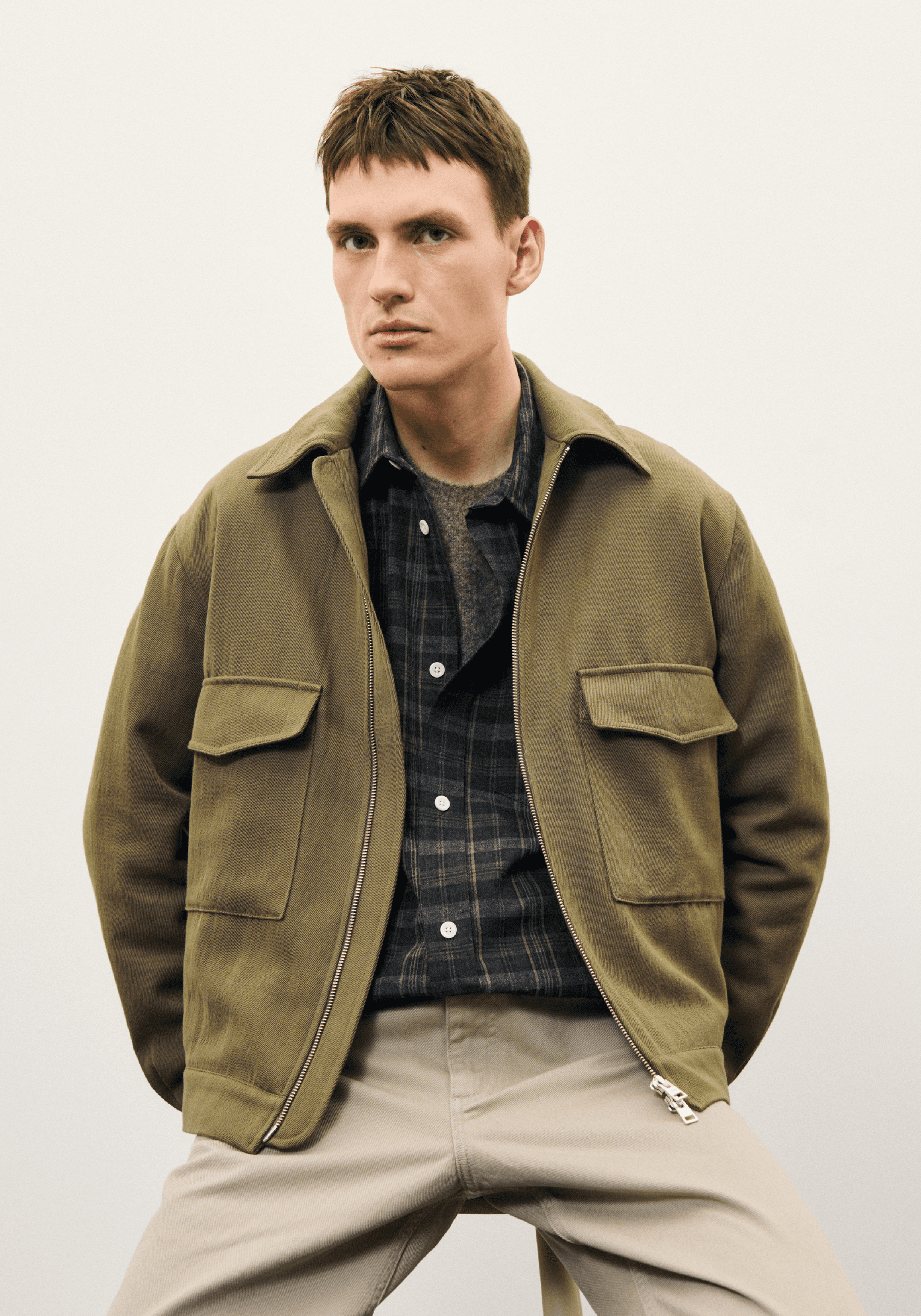 Homme portant un blouson en laine verte, un pantalon beige et une chemise à carreaux dans le lookbook de Norse Projects
