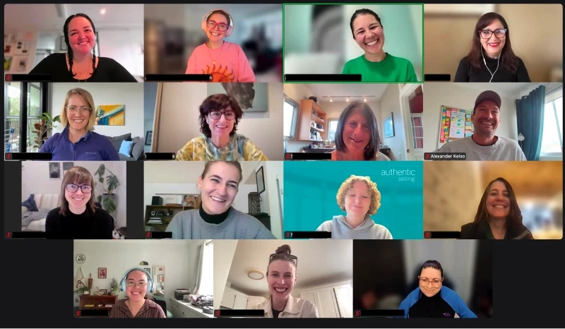 A group of fifteen people smiling and participating in an online video conference, each in their own square as part of a grid layout, with a mix of home and office backgrounds, reflecting a lively and diverse virtual meeting.