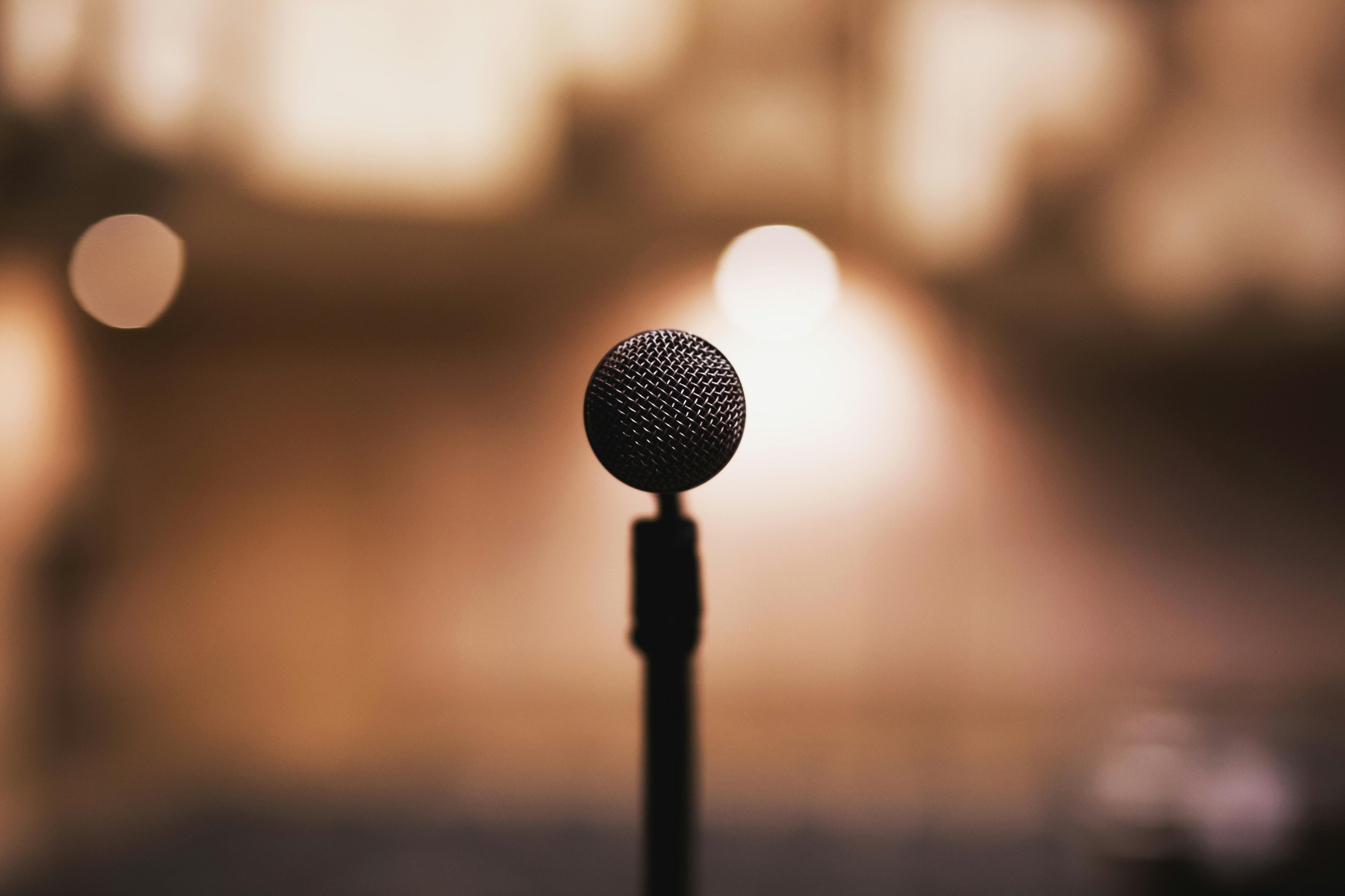 An image of a microphone, the backgroudn blurred, but showing an event venue environment.