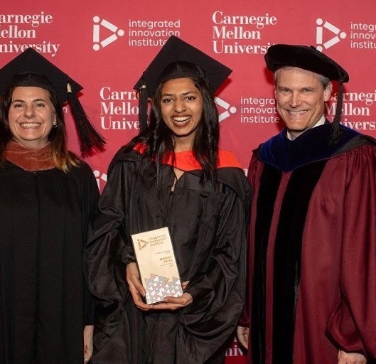 Jahnavi holding the Changemaker Award at the Carnegie Mellon graduation ceremony, between two professors