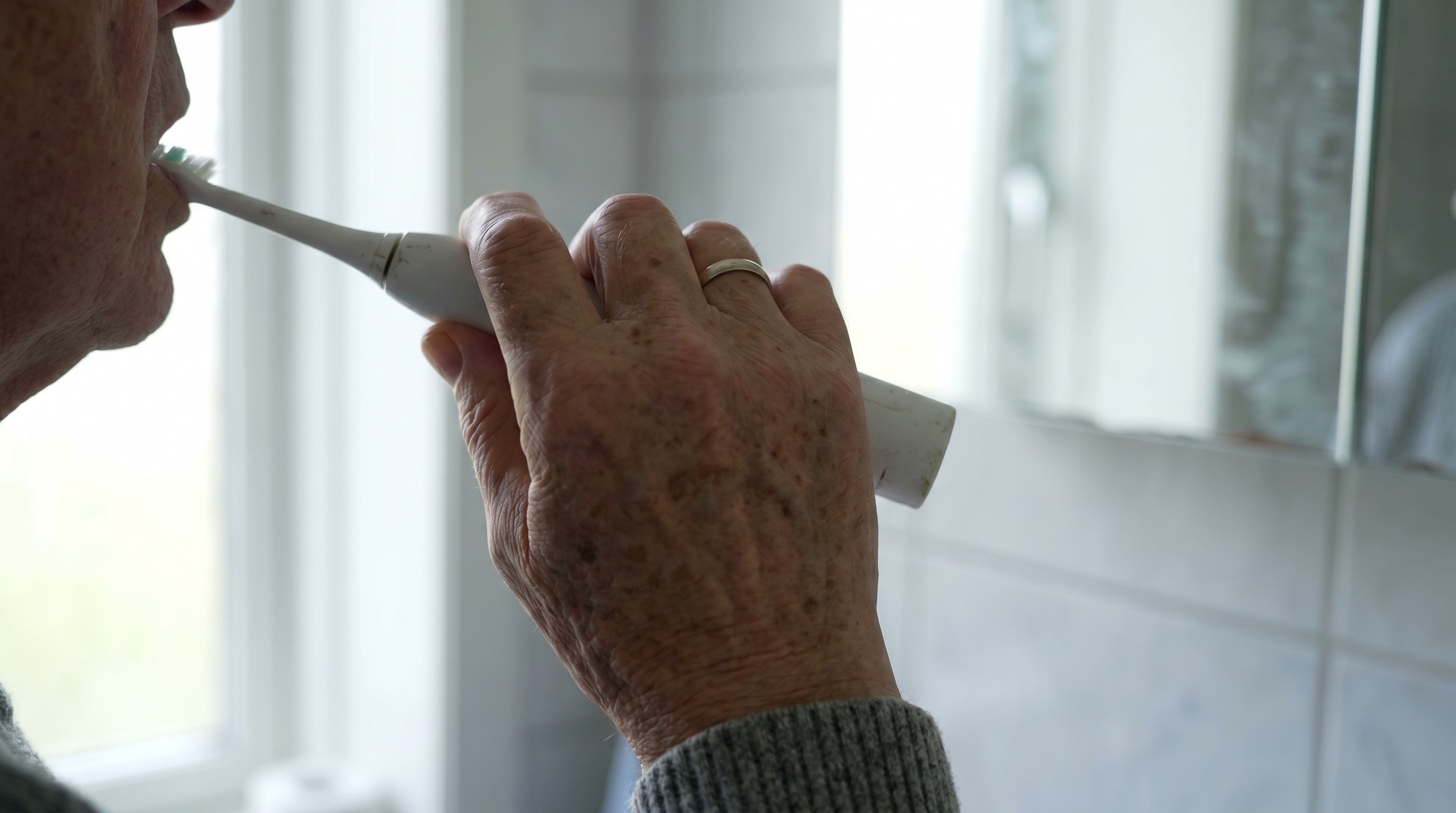 Older adult holding an electric toothbrush near the lower jaw in soft morning light