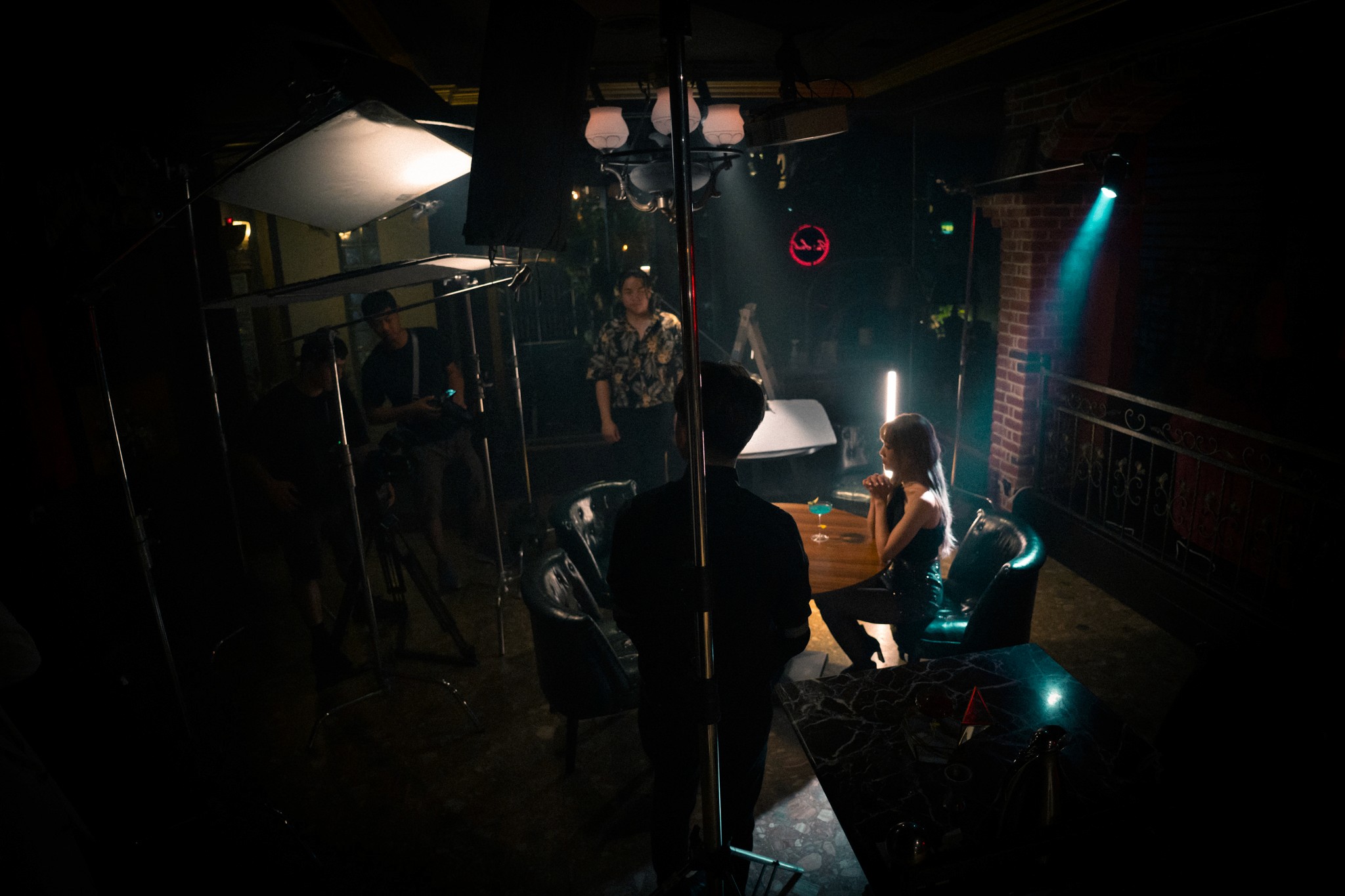 Two filmmakers operate a large camera on a dimly lit set. One wears headphones, both focused, suggesting a serious, creative atmosphere.