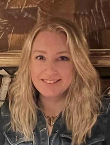 Portrait of a smiling blonde woman in a denim jacket in front of a wooden panel