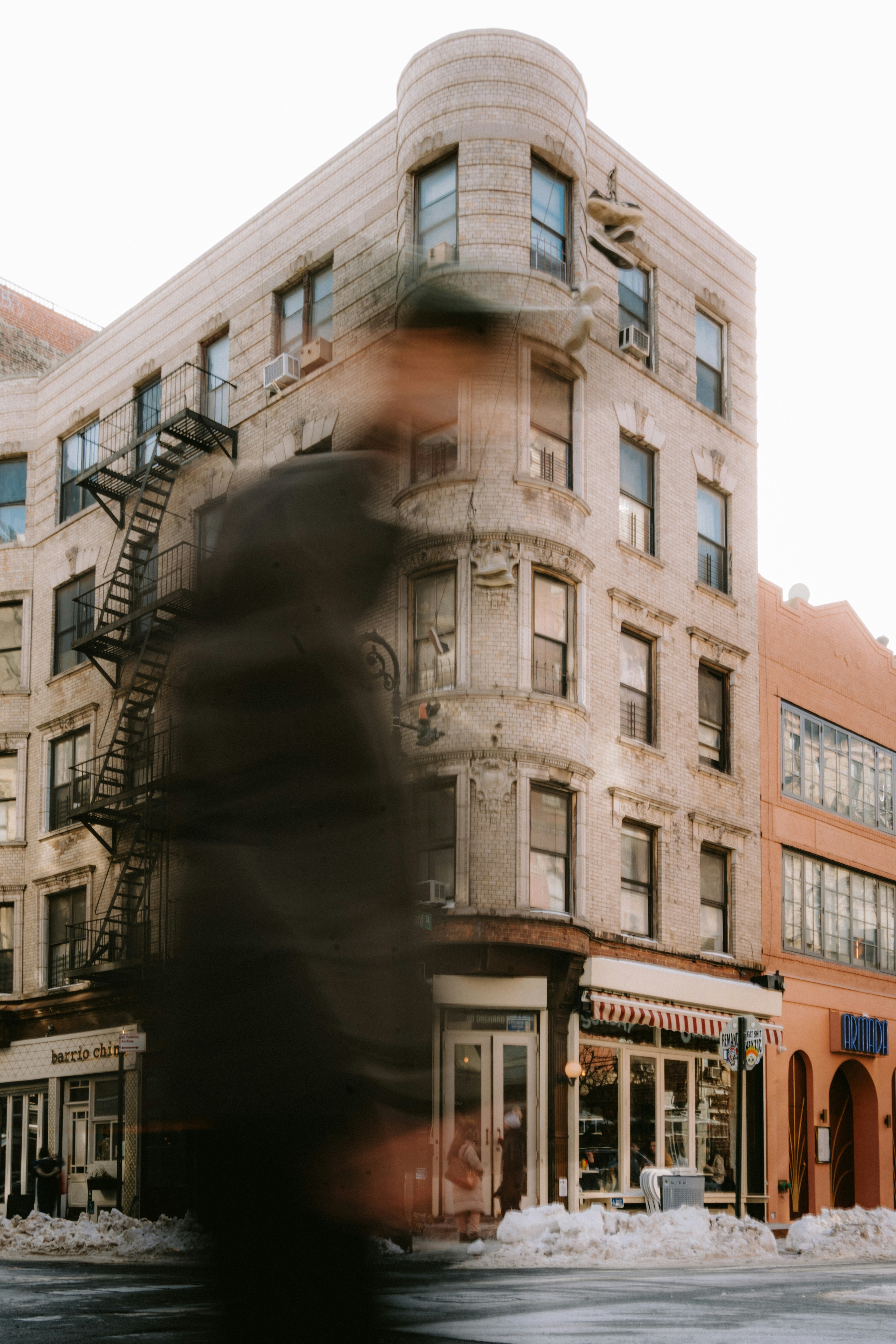 Blurry figure walks past a building with fire escape.