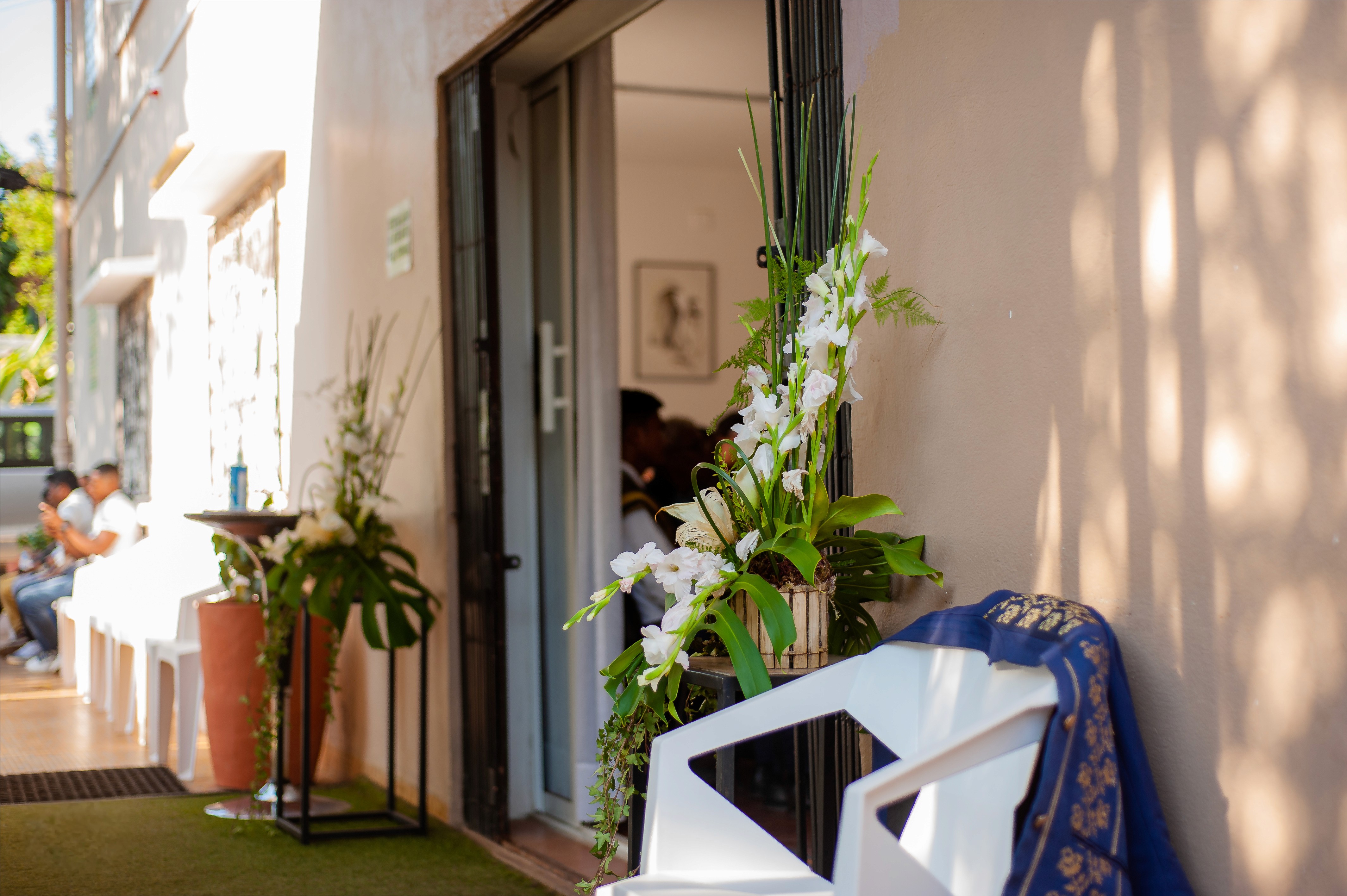 Entrée décorée avec des fleurs blanches, des chaises blanches et des invités assis en arrière-plan lors d'une cérémonie en plein jour.