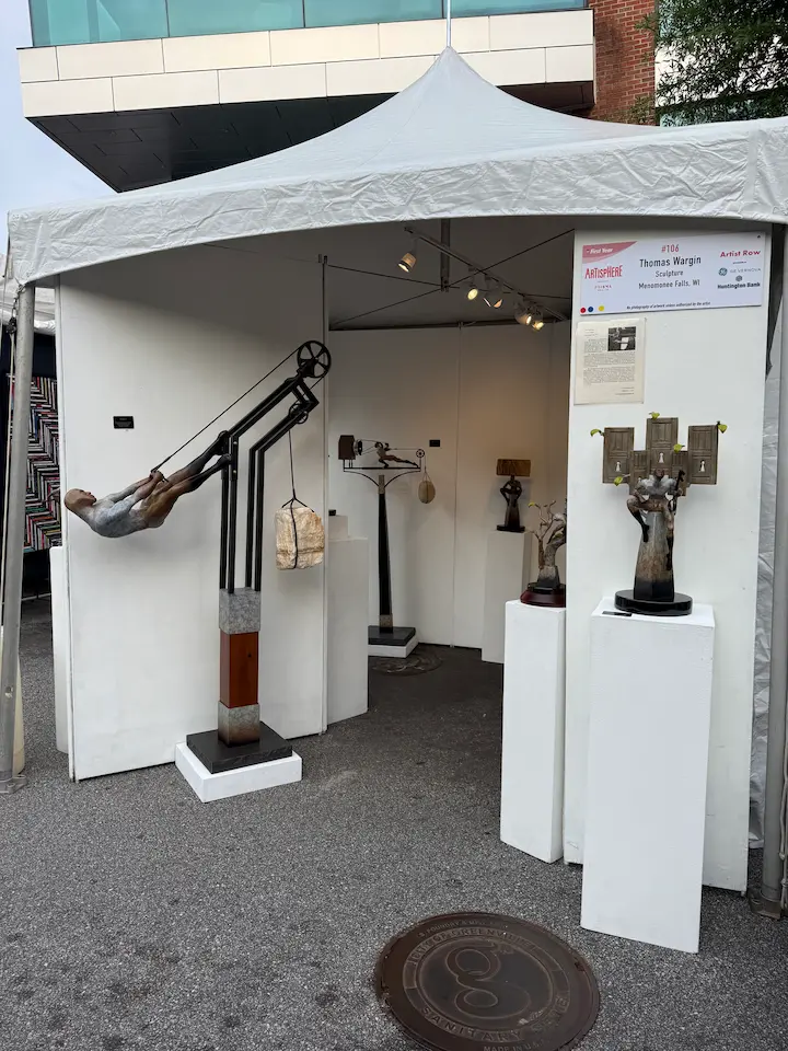 Contemporary sculpture display at Artisphere in downtown Greenville featuring abstract human figures and kinetic-style artwork inside a white artist booth.