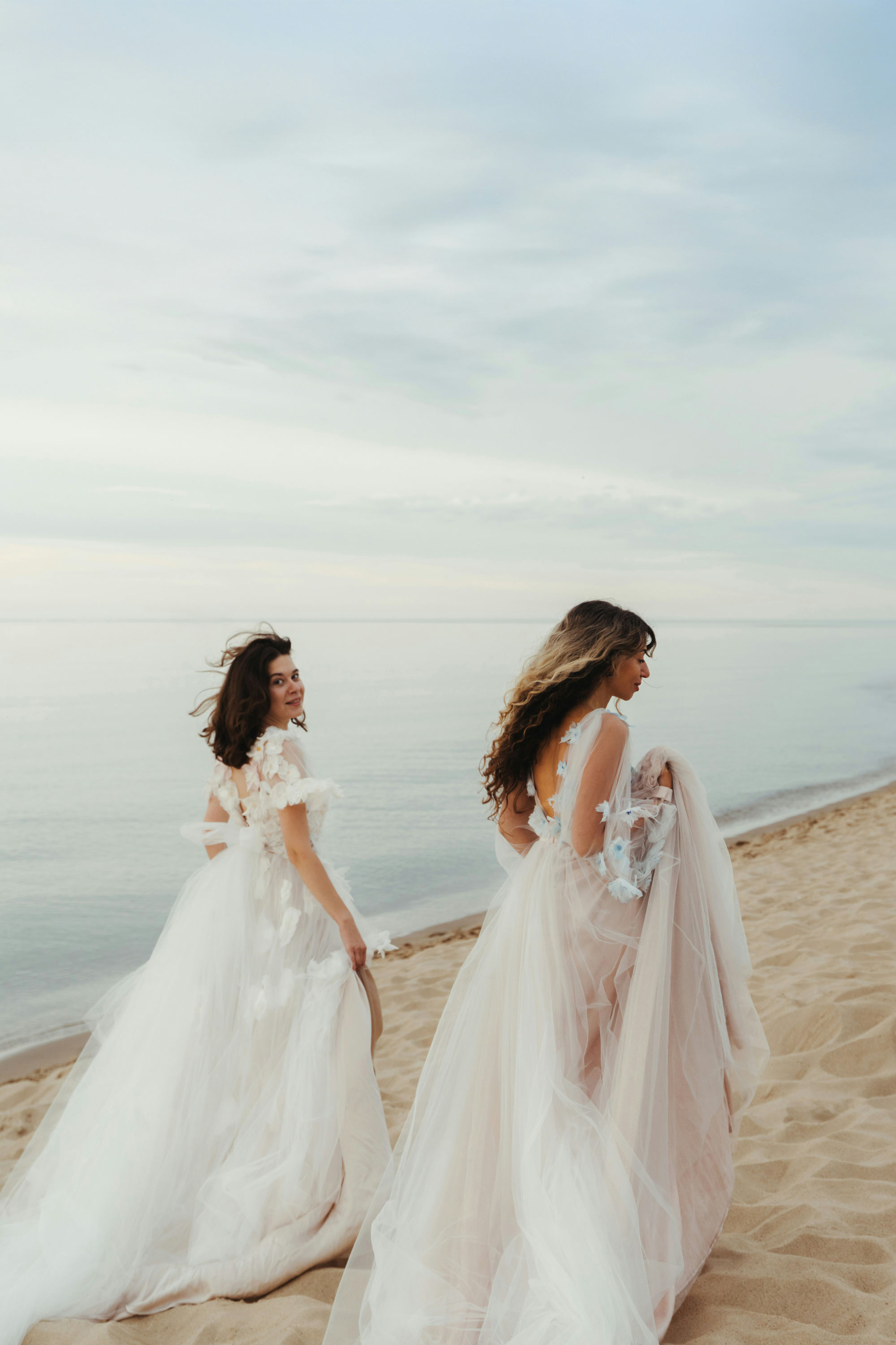 Two women on the beach wearing wedding dresses