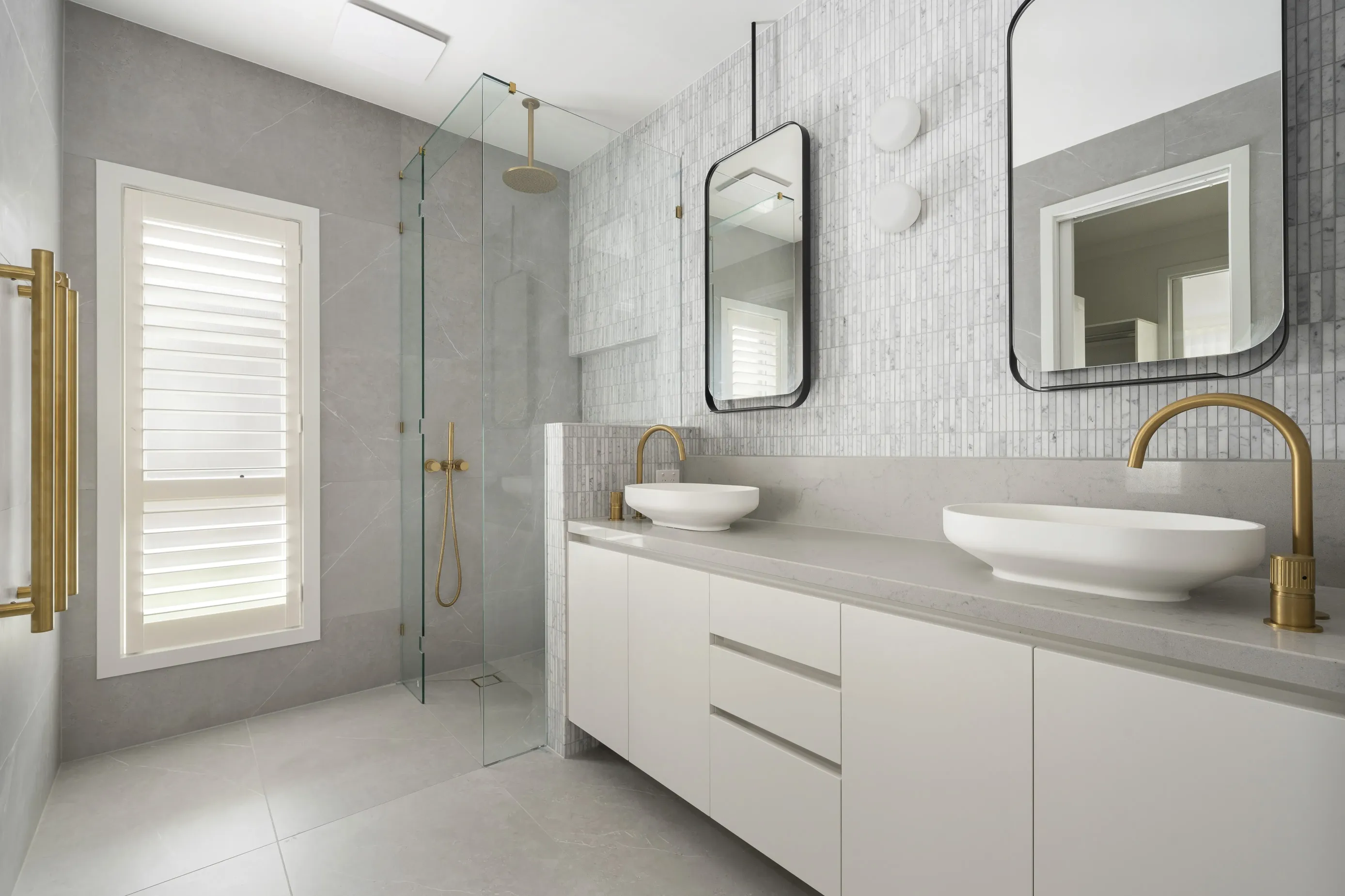 Bundoora ensuite with a glass walk-in shower, twin vessel basins, brass tapware and a vertical mosaic feature wall