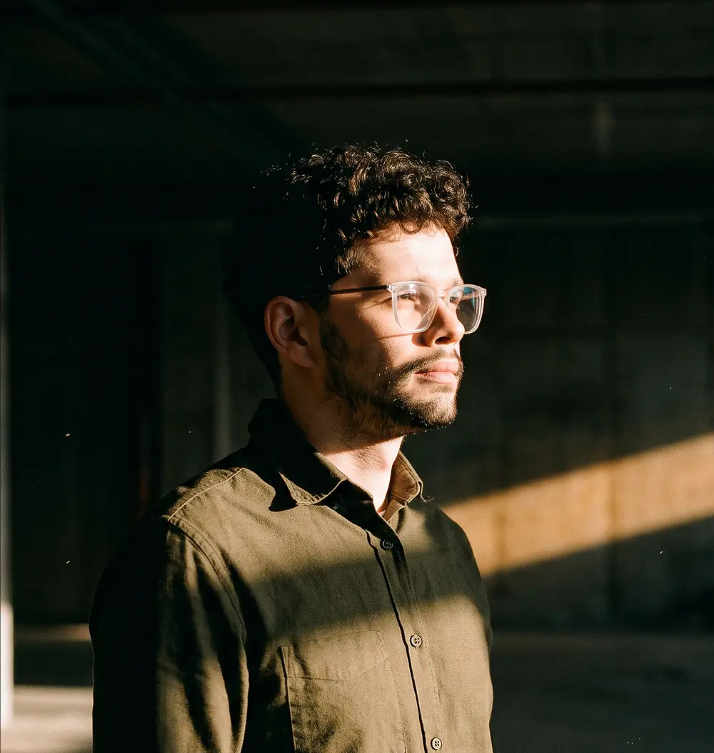 Michal Palenčár, UX/UI Designer, wearing glasses in warm studio light.