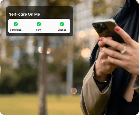 Two smiling people outdoors, one in a pink jacket holding a white phone, the other in blue with a buzz cut holding a blue phone, under a clear sky.