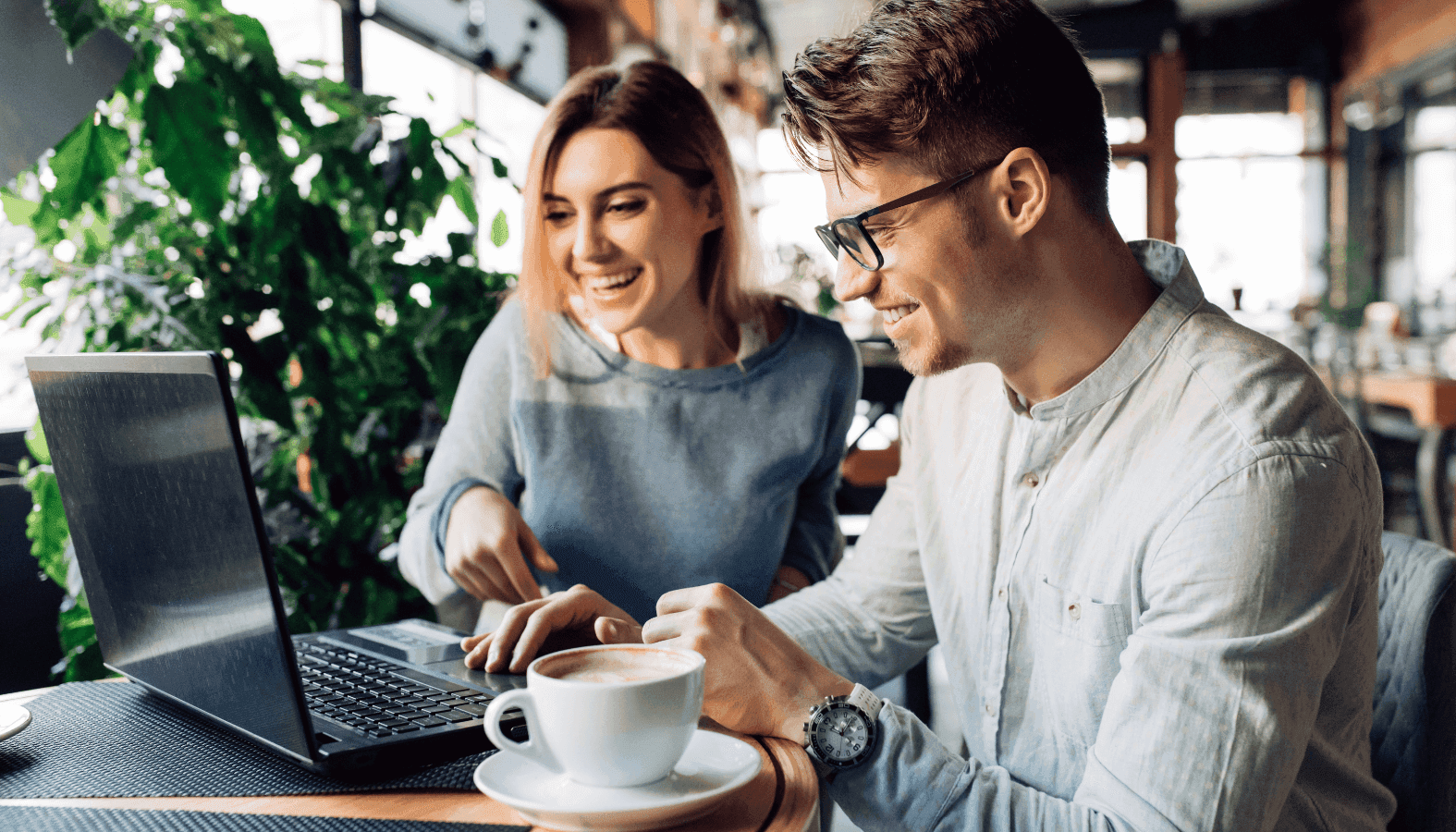 couple sitting cheerfully looking laptop screen