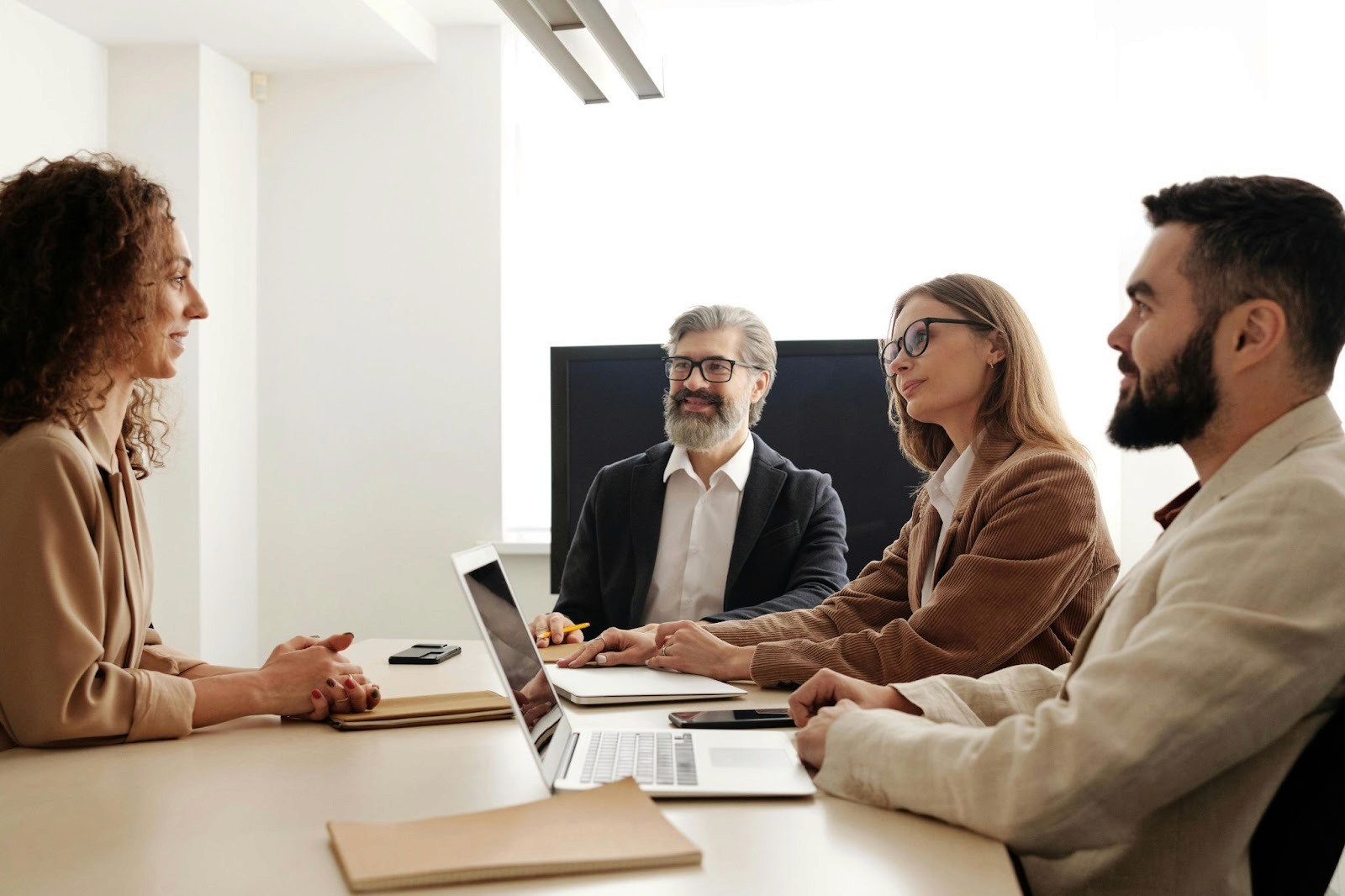 Two women and one man sitting around a desk at work. There is a laptop on the desk and also some paperwork. They are in an office space.