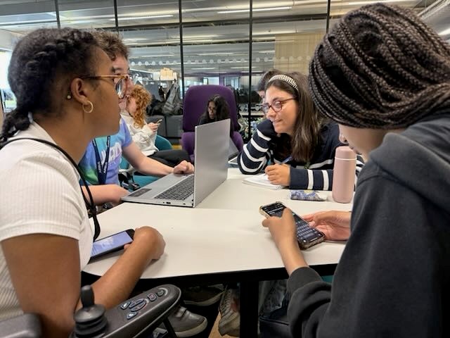 Image of young people at the event around a table talking stragegy as part of a creative workshop