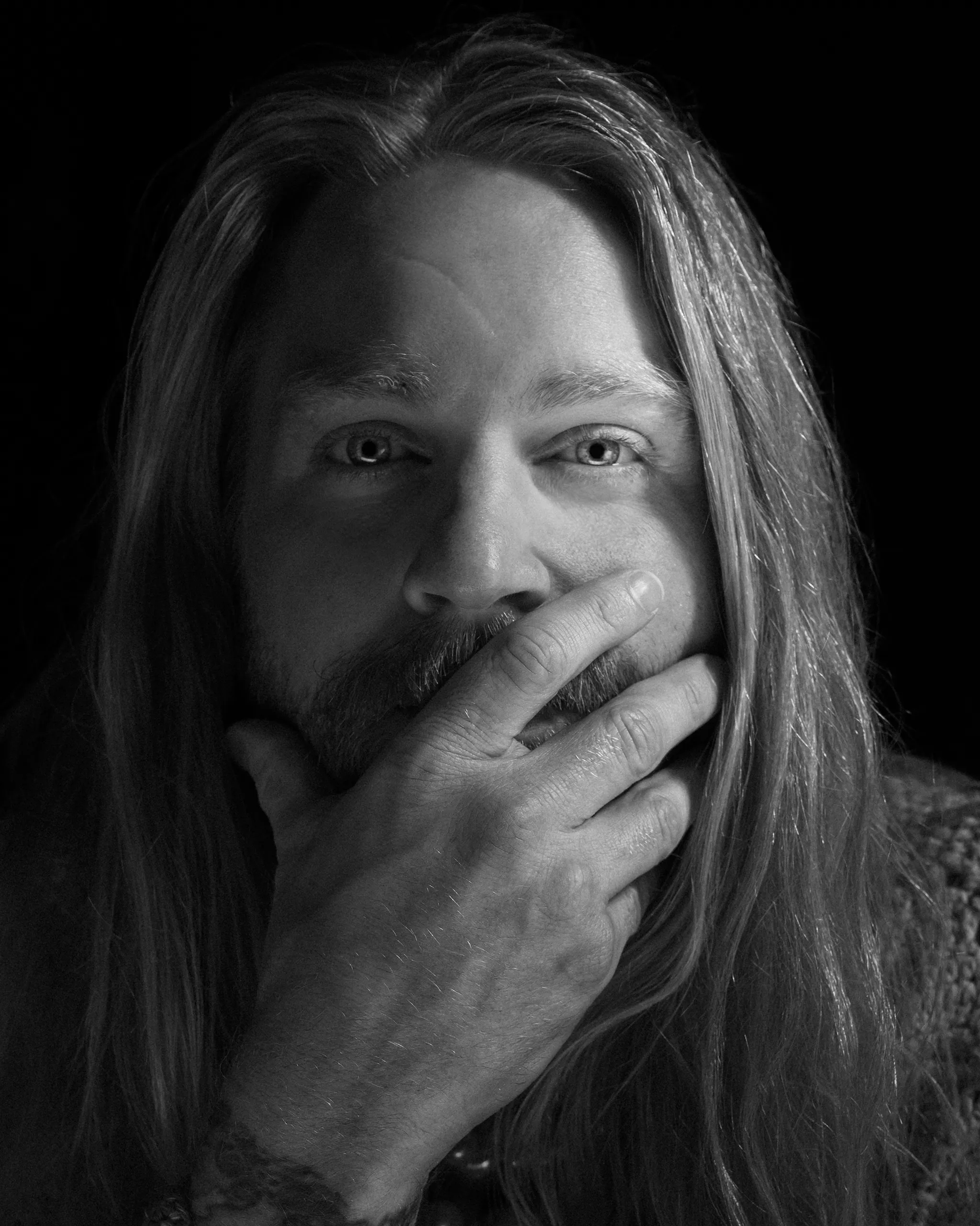 Close up black and white portrait of Sam Ryder with his hand over his mouth.