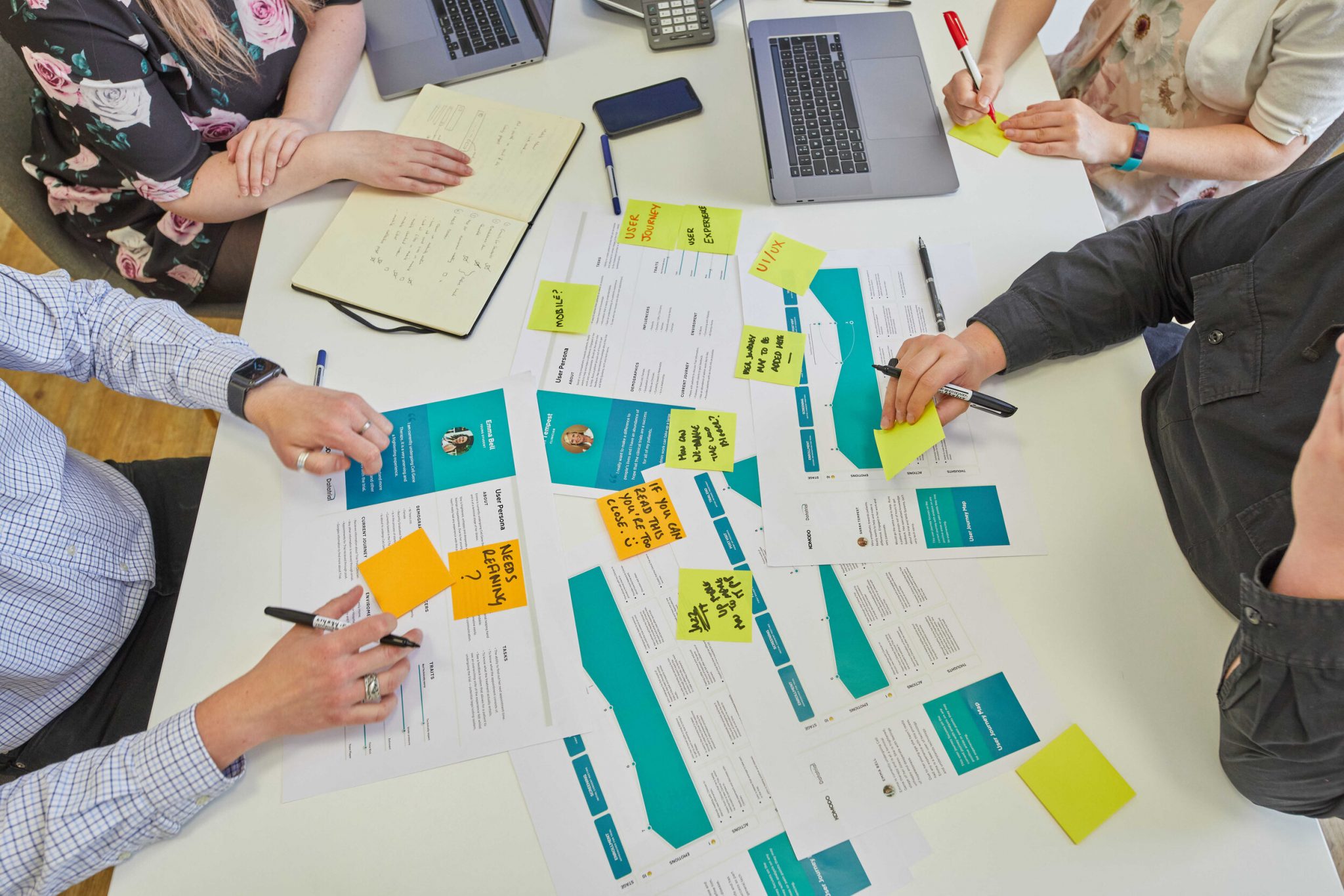 Bird's eye view of a workshop in the Komodo studio. People are sat around a table writing on brightly coloured post-it notes.