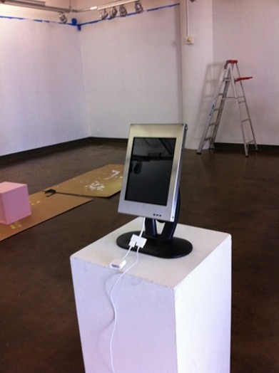 A photo of a pc screen with white cables put on a white cubical pedestal.
