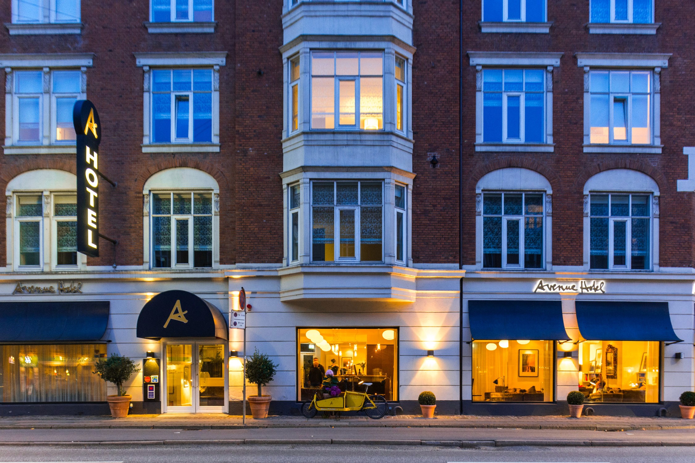 A brick building with two storefronts, "Avenue" and "Avenue Cafe," featuring large windows and a central bay window.