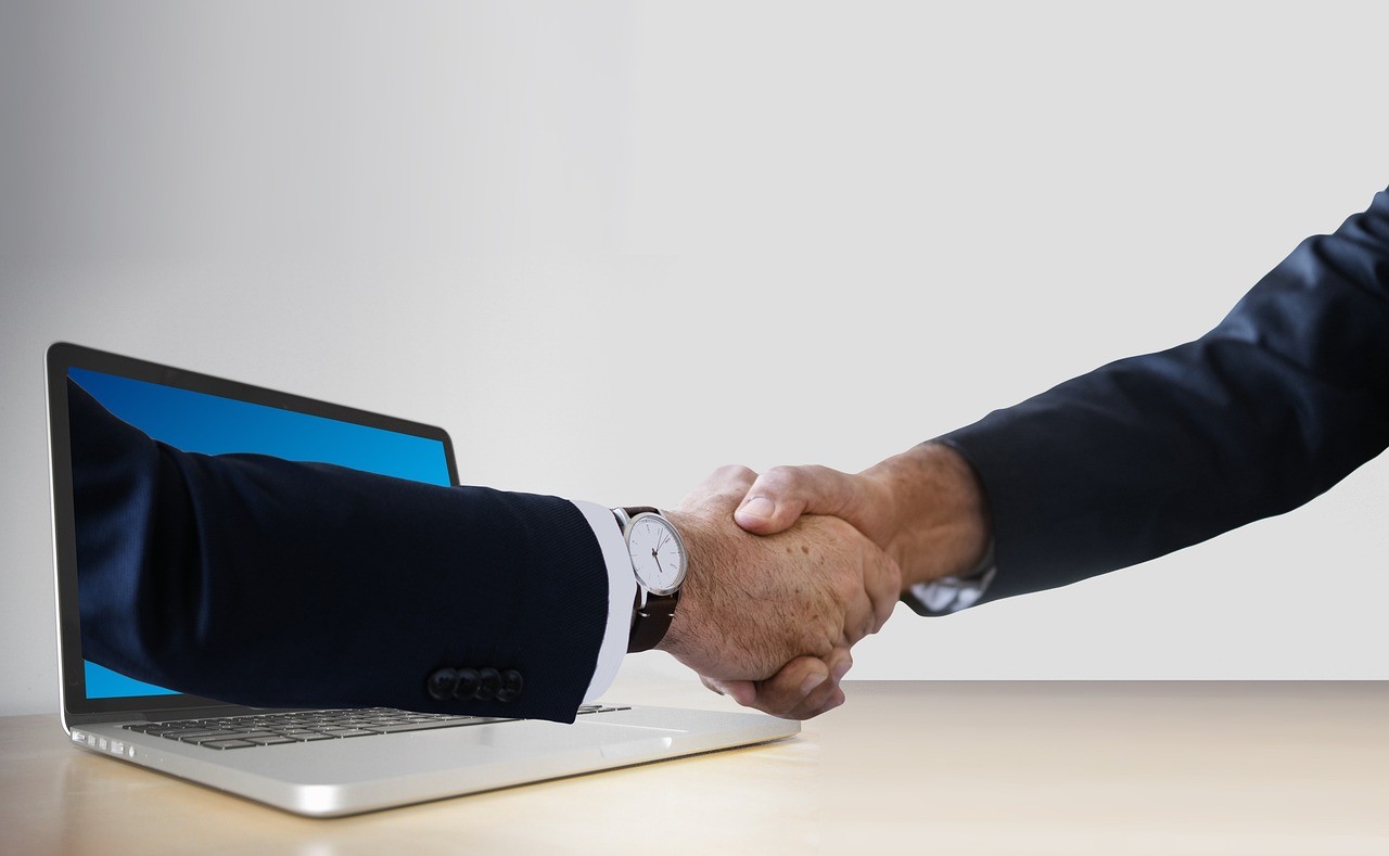 Handshake emerging from laptop symbolizing digital collaboration