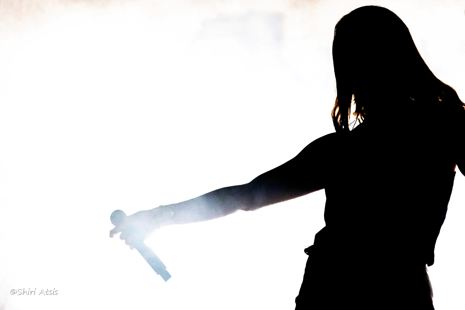 צילום סילואט (צללית) דרמטי של מרינה מקסימיליאן בלומין במהלך הופעה חיה. הזמרת נראית כדמות כהה אוחזת מיקרופון על רקע לבן ומואר בעוצמה, לכידת רגע אמנותי על הבמה מאת Shiriz Photography. הצלמת שירי עציץ