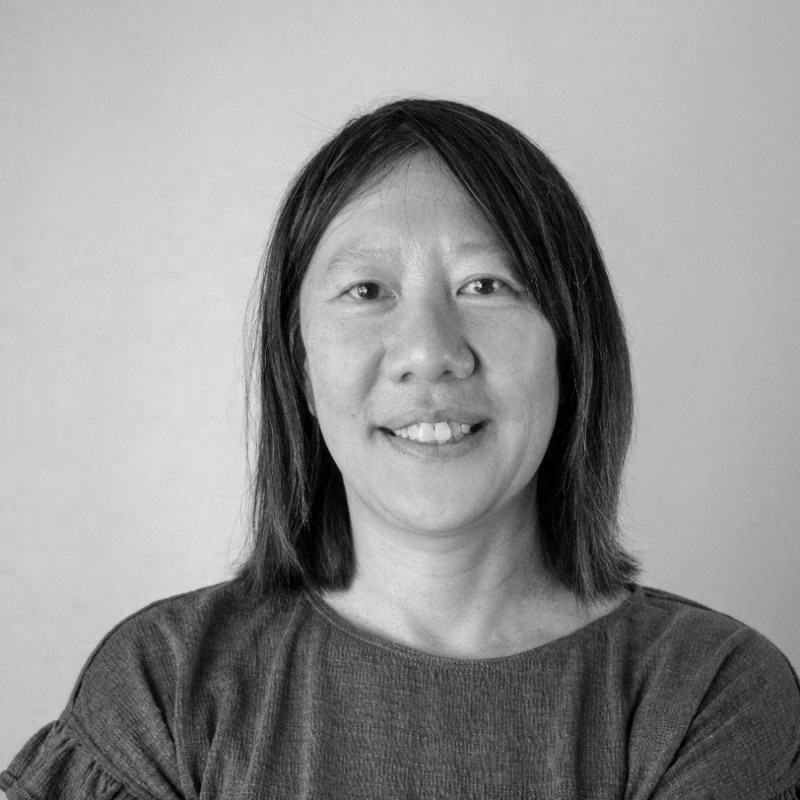 A thoughtful young person with dark hair gazes to the side, captured in soft black and white lighting.