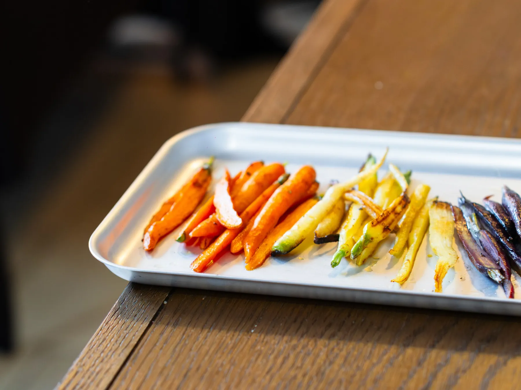 A tray of roasted rainbow carrots on an oak table