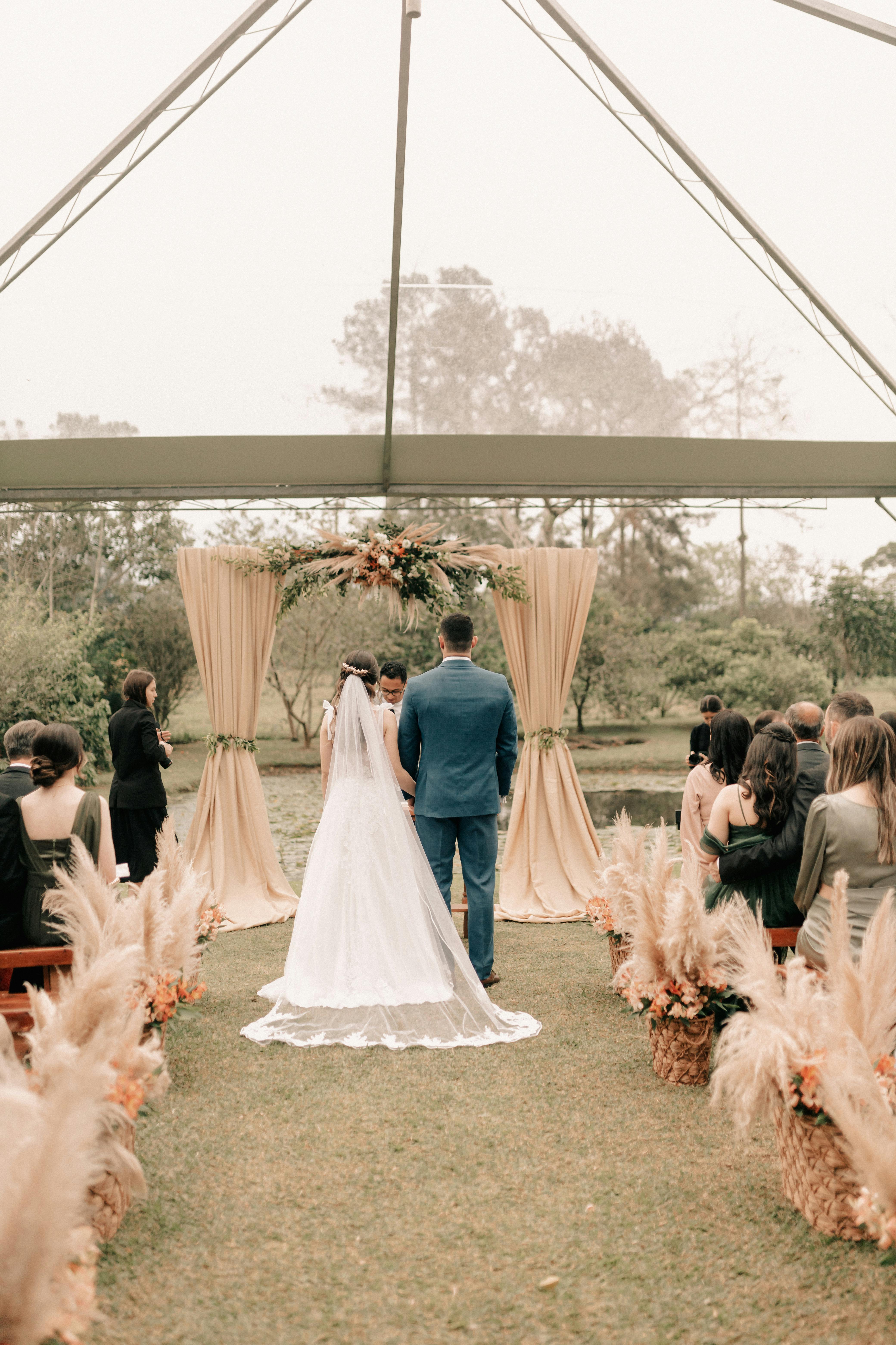 A couple in wedding attire walks hand in hand across a sunlit field.